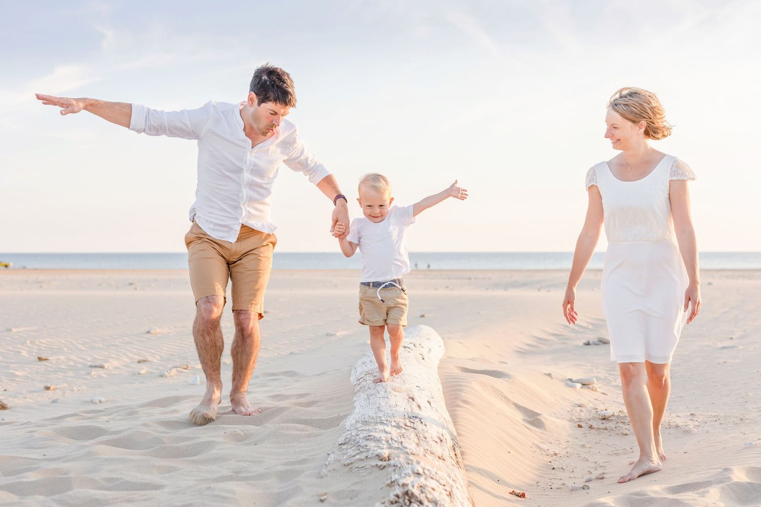 Family walking and balancing together on a sandy beach ridge during a seaside photoshoot.