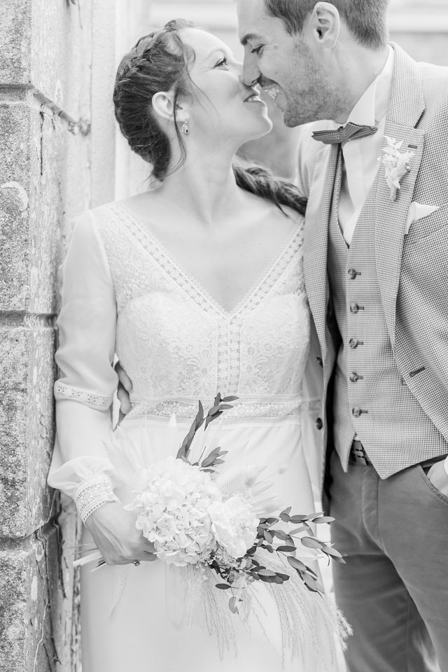 Wedding couple in vintage attire sharing tender moments against white stone wall.