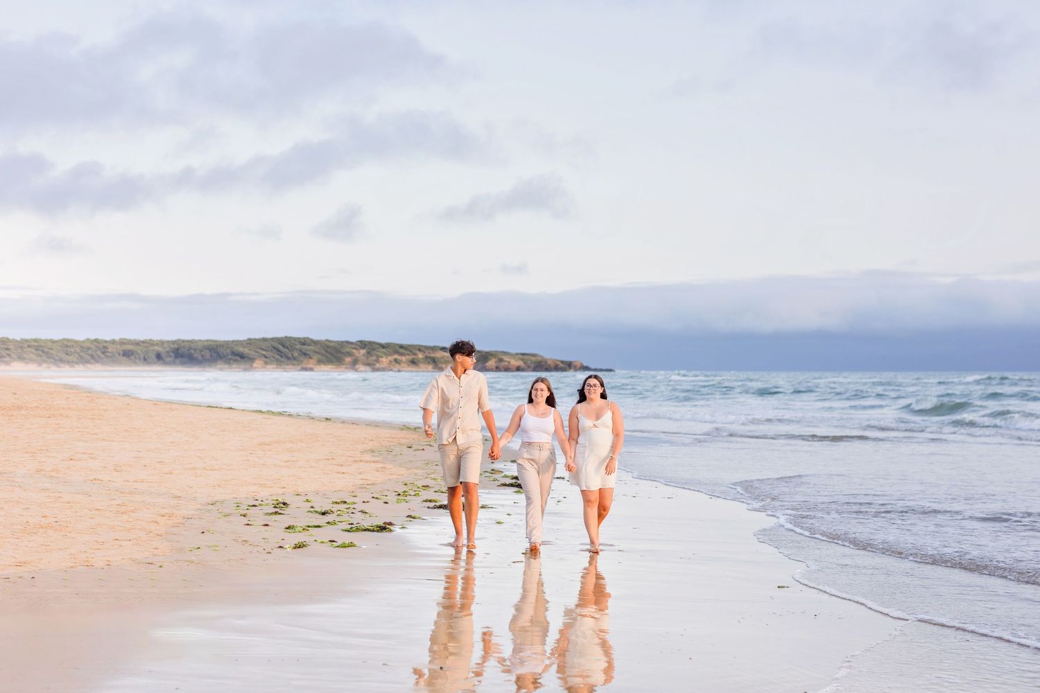 Three people walking along a scenic beach at sunset with ocean waves in the background.
