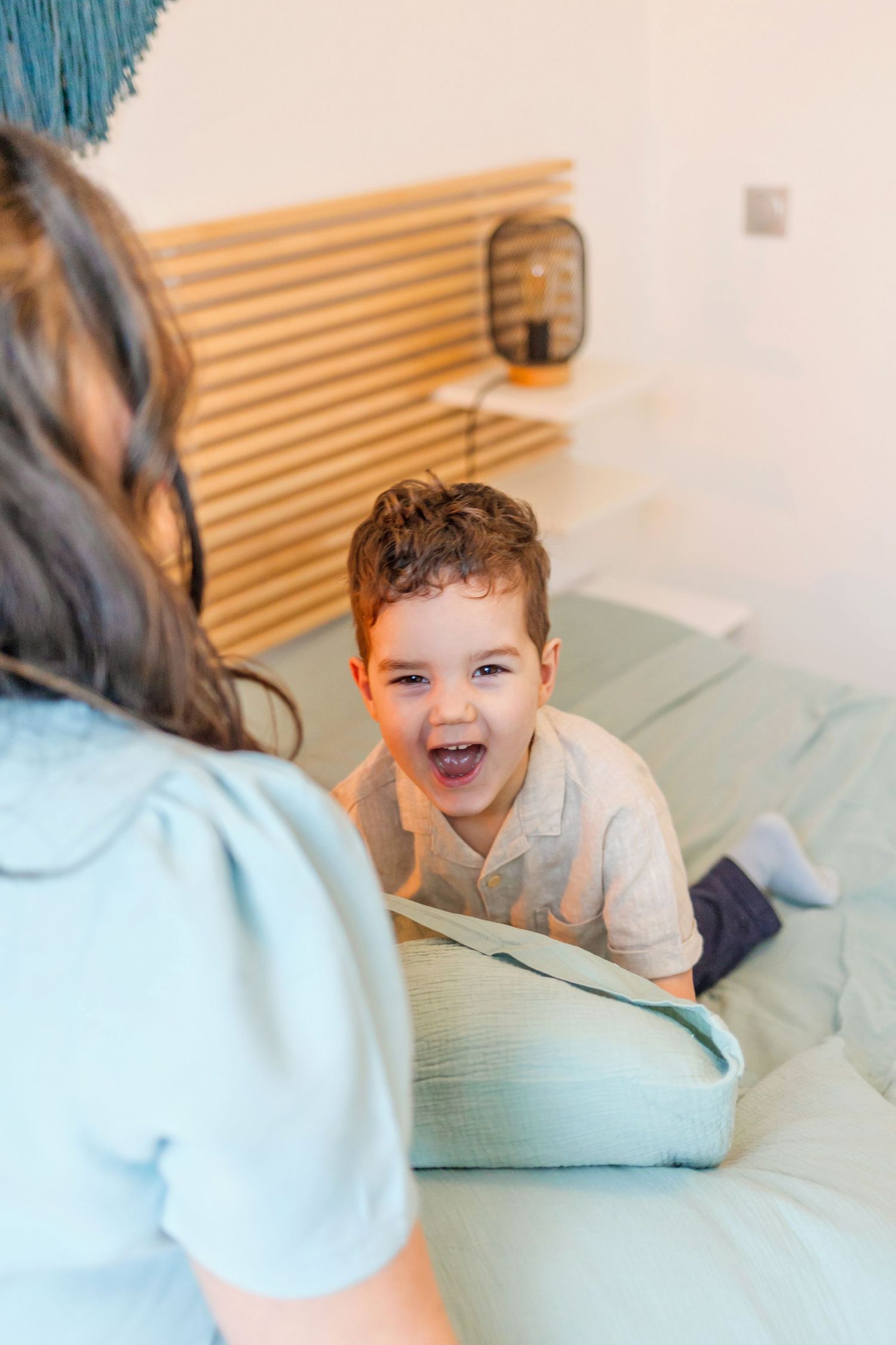 A joyful play session on a bed with mint green pillows and wooden headboard decor.