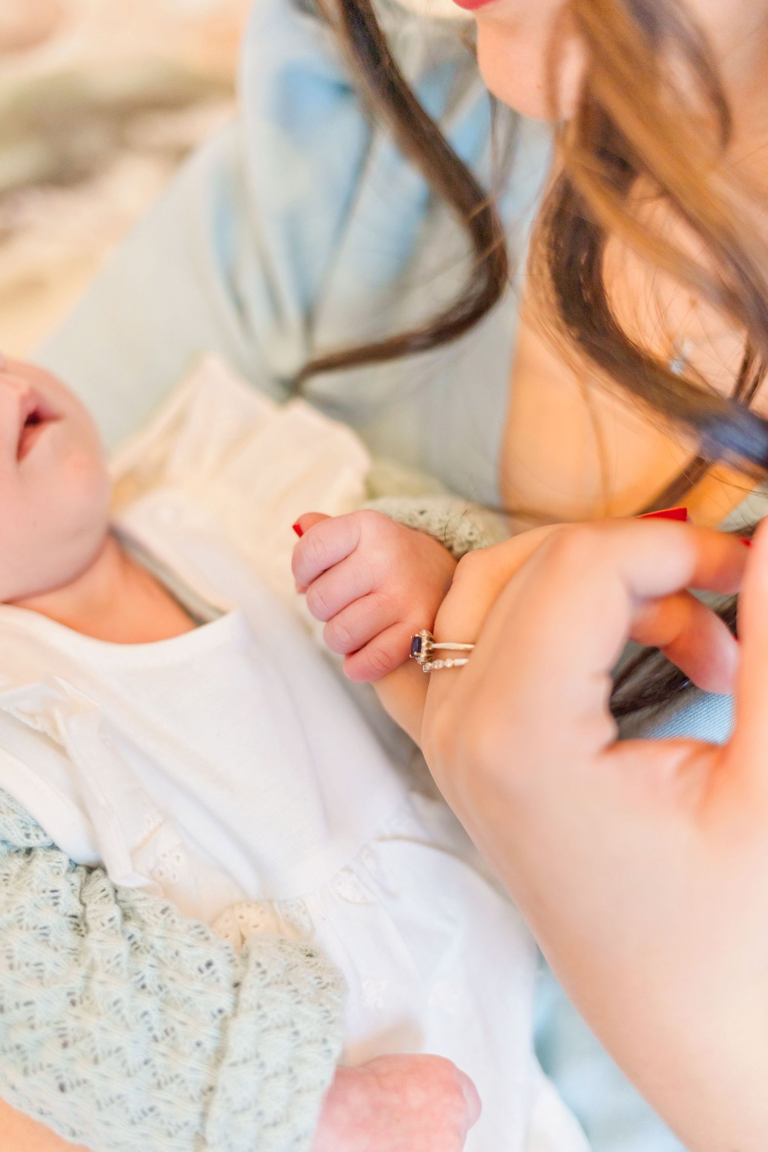 Close-up shot of gentle hands holding a newborn baby wearing white against a soft background.