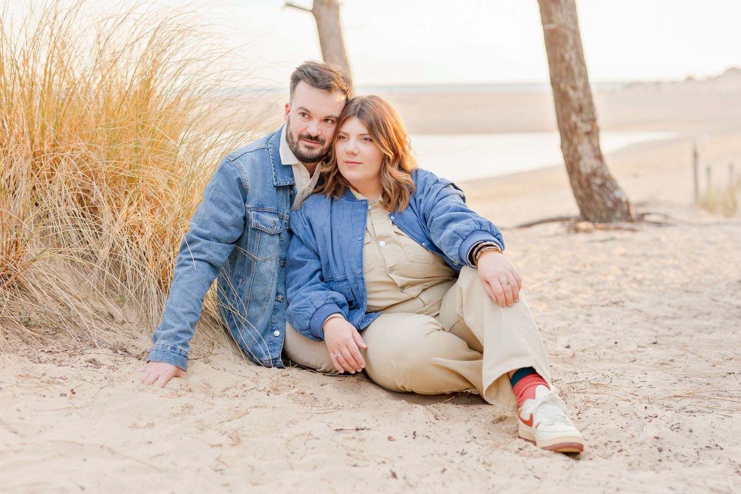 Couple in denim and khaki relaxing on sandy beach during golden hour.