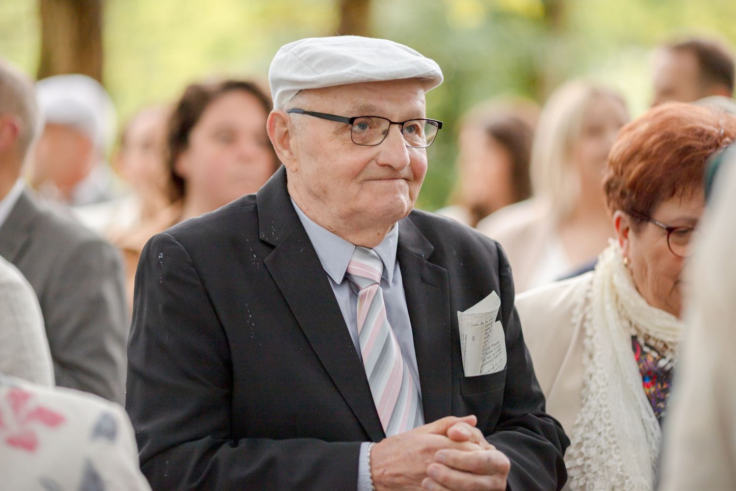 Guest in formal attire observing an outdoor wedding ceremony with a thoughtful expression.