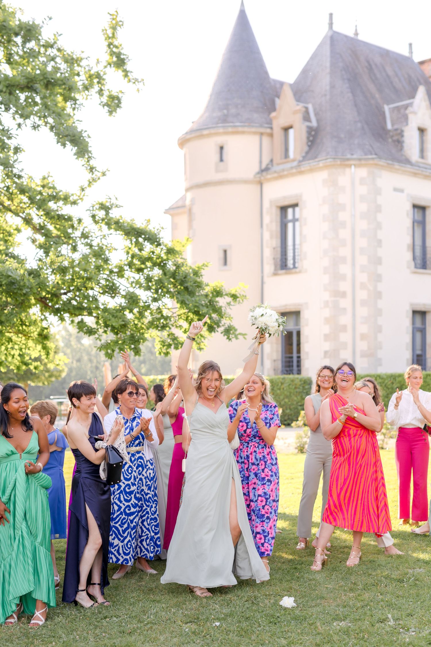 Wedding celebration group shot with guests wearing bright summer dresses outside historic venue.