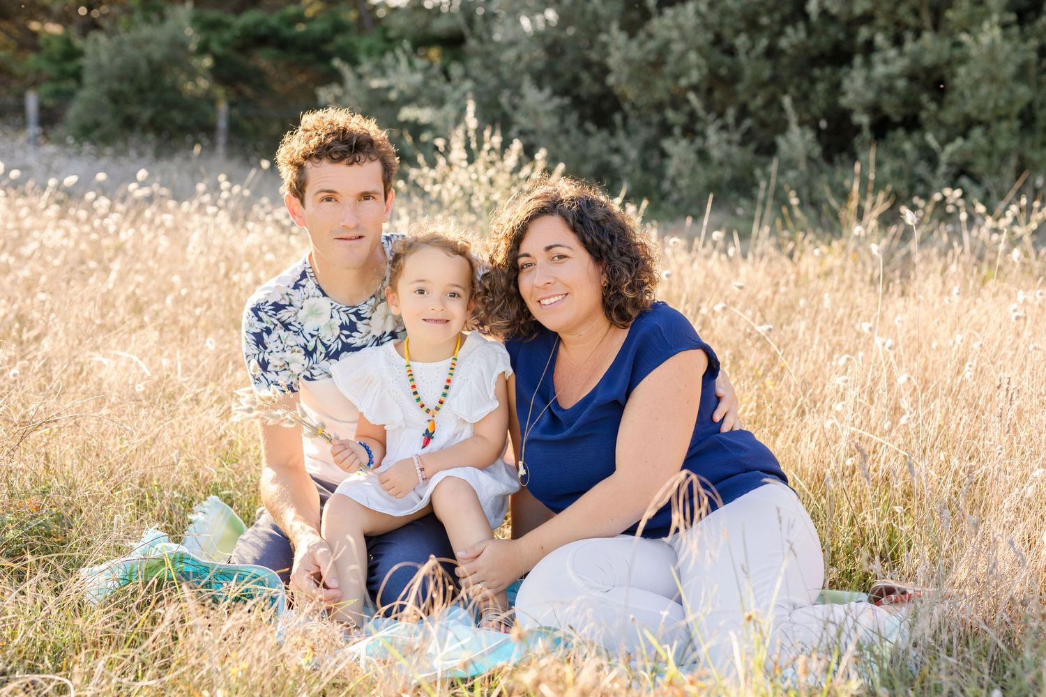 Family sitting together on blanket in golden field during sunset photoshoot.