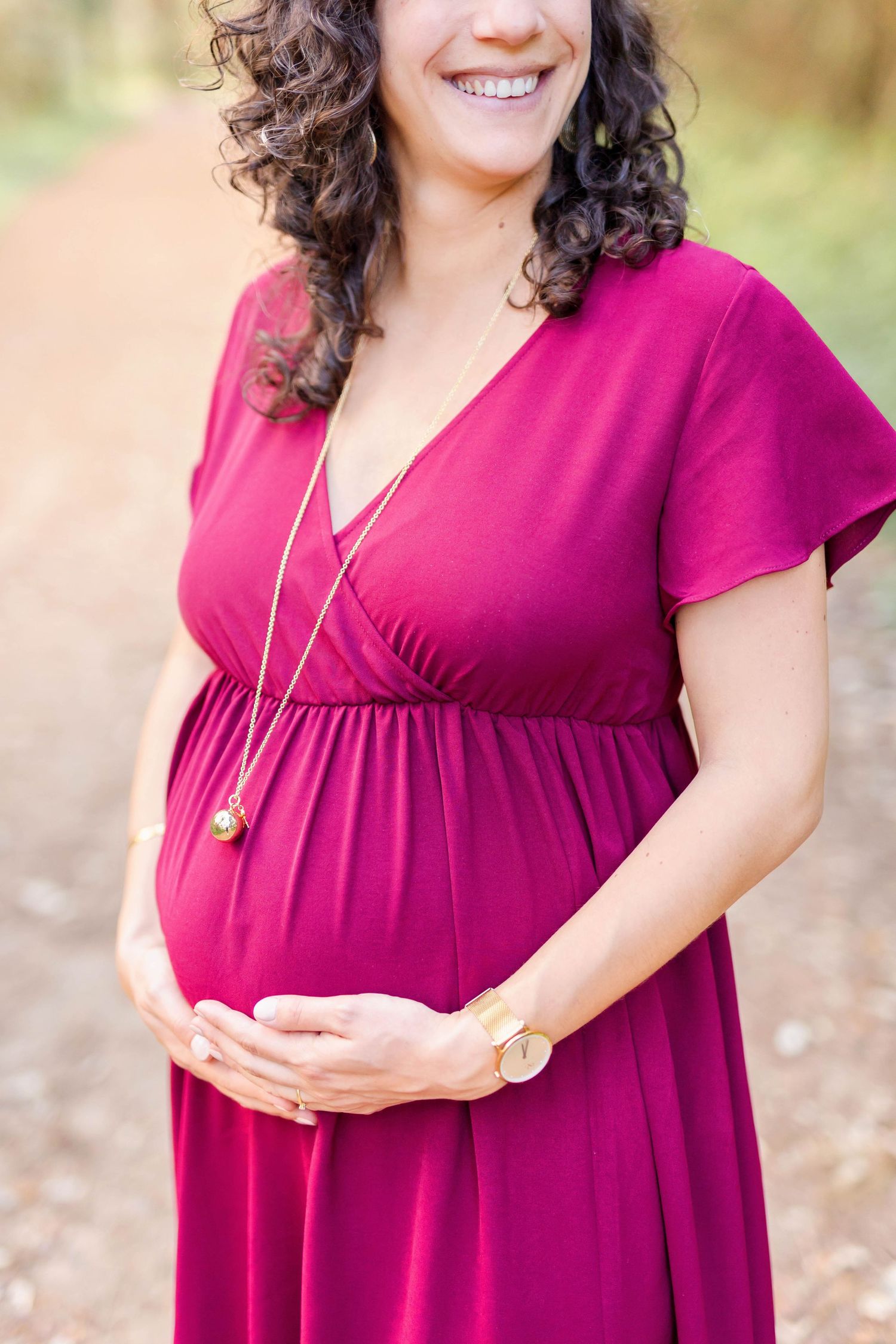 Close-up shots of a pregnant woman in a flowing burgundy dress posing in natural outdoor lighting.