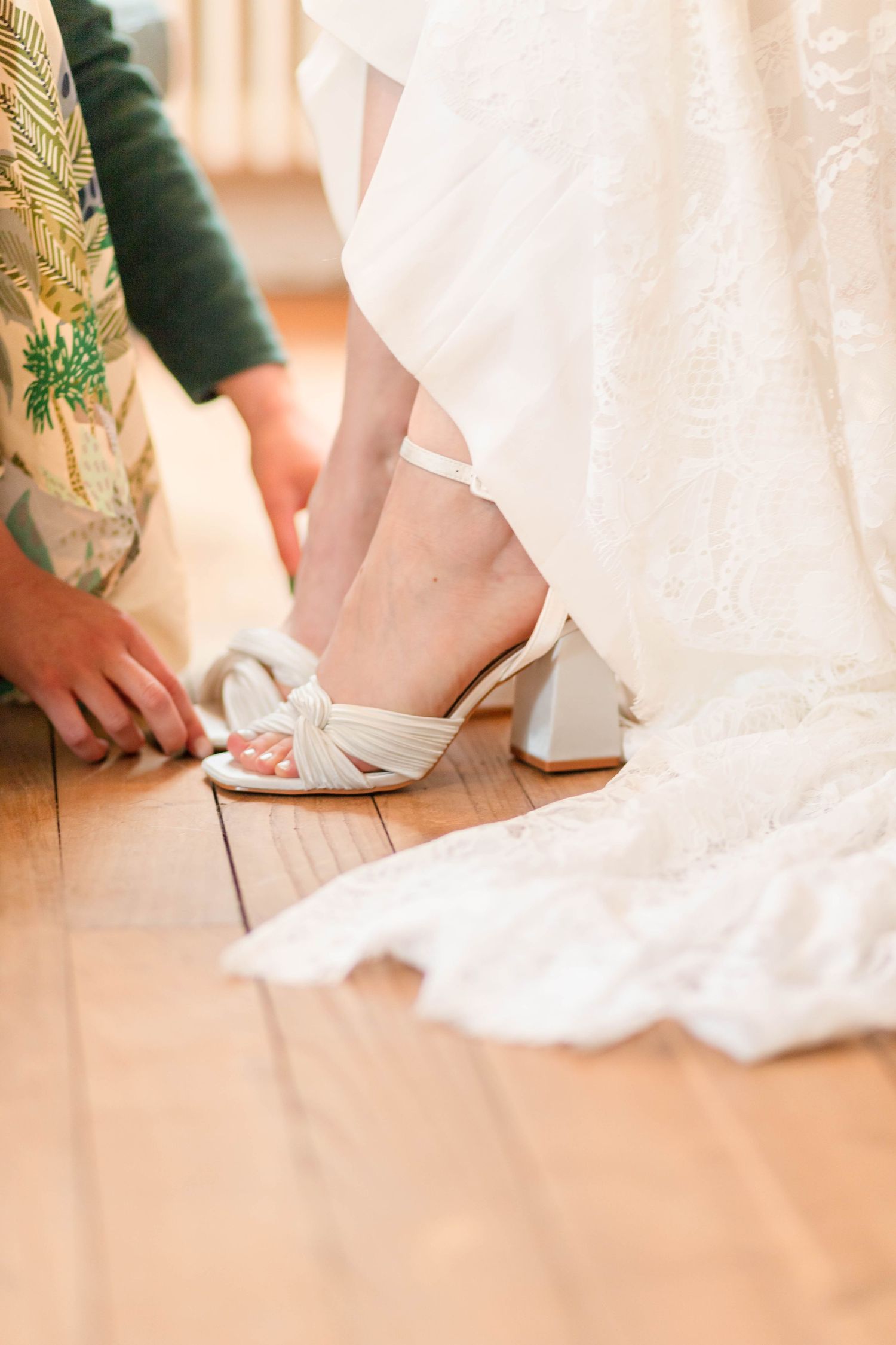 White wedding shoes and dress hemline shown against a light wooden floor.