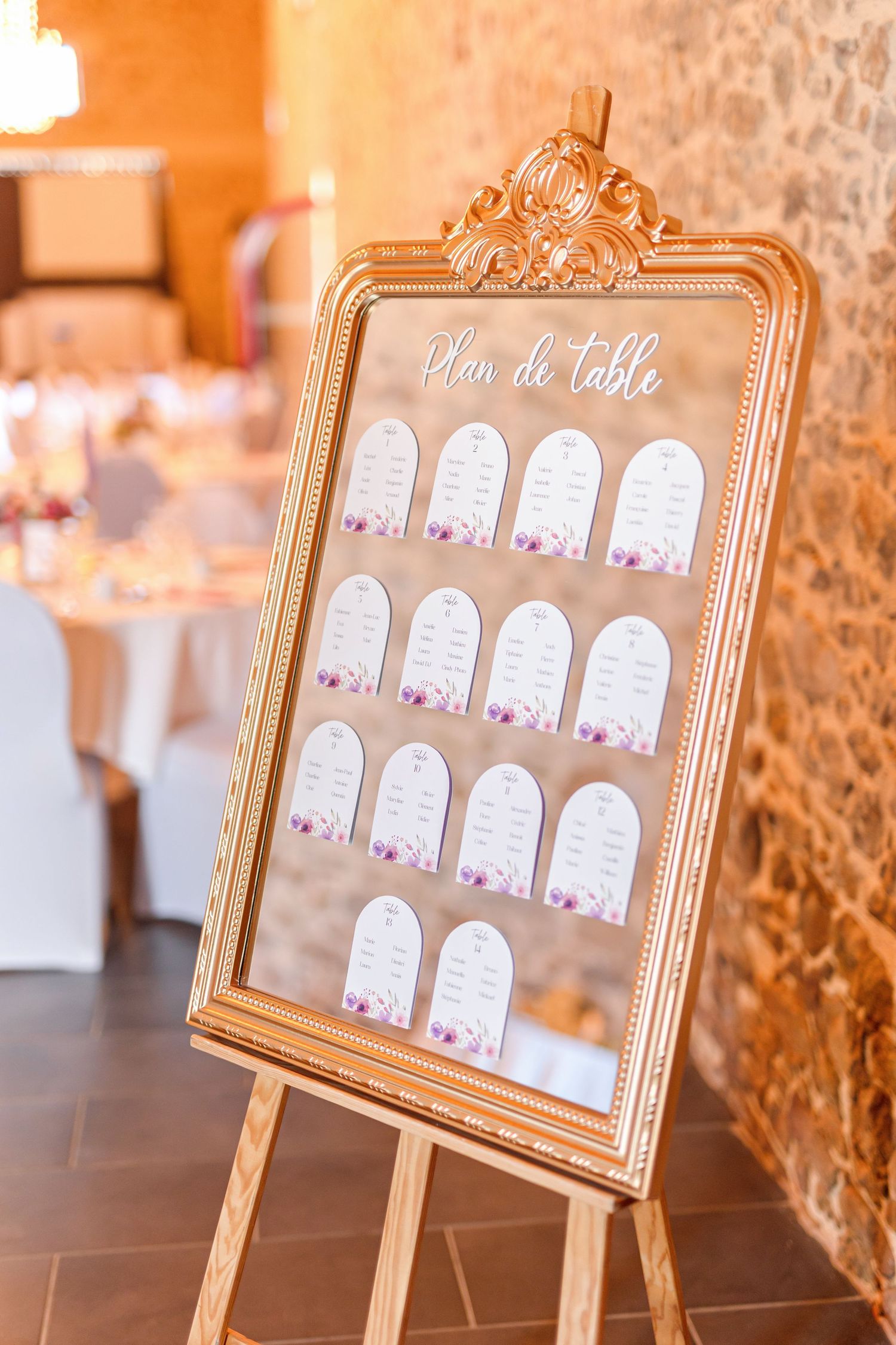 Elegant gold-framed seating chart display with floral decorated cards arranged on an ornate easel at a wedding reception.