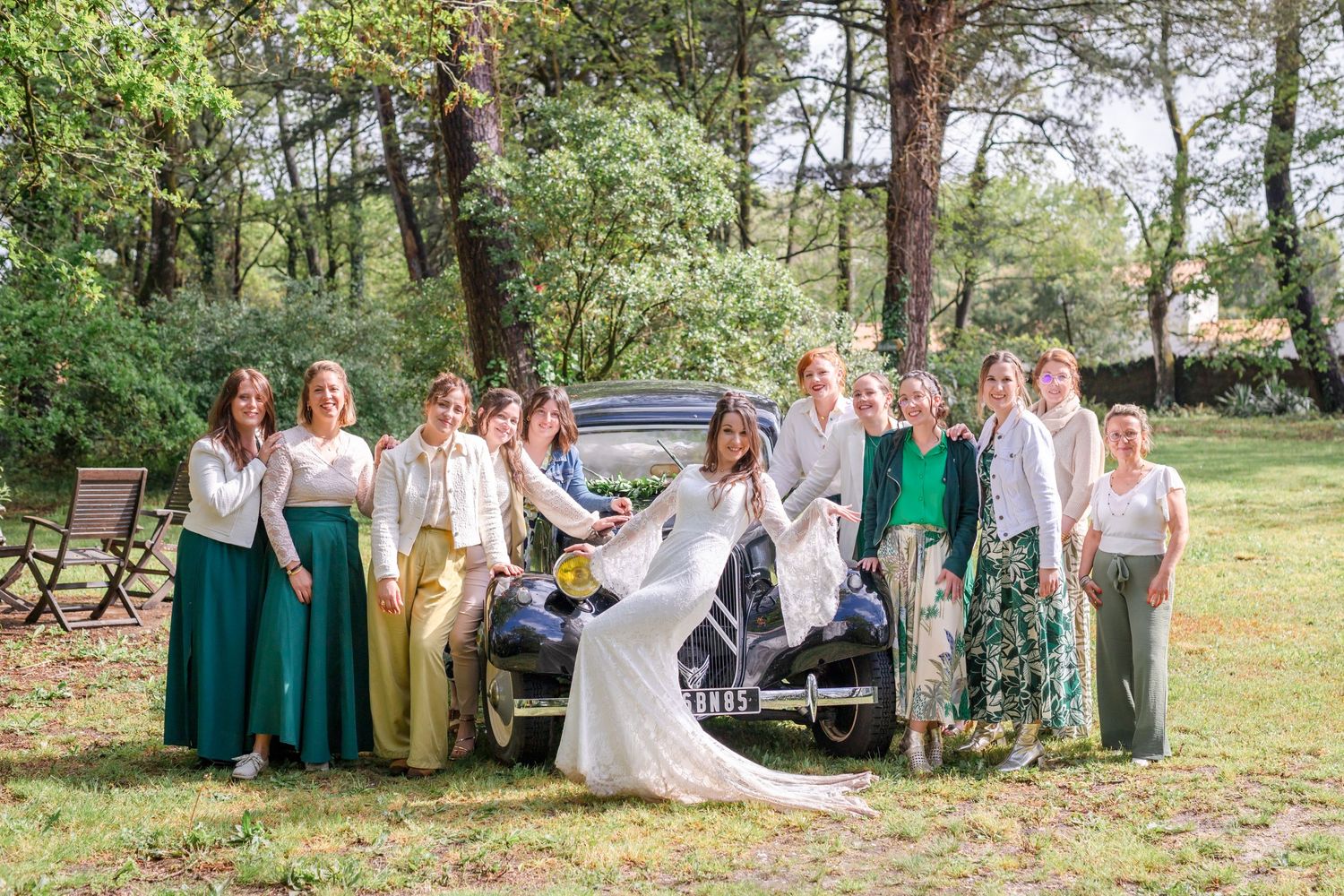 Wedding party gathered outdoors on a sunny day wearing elegant green and neutral colored attire.