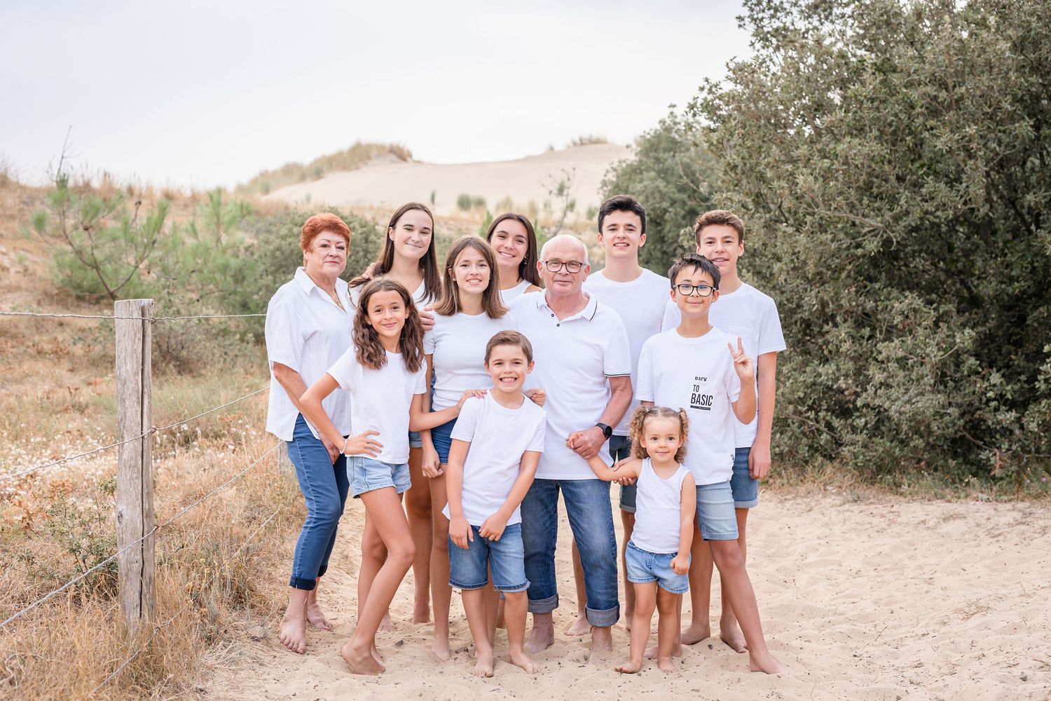 Extended family posing together on a sandy path surrounded by green foliage wearing matching white and denim.