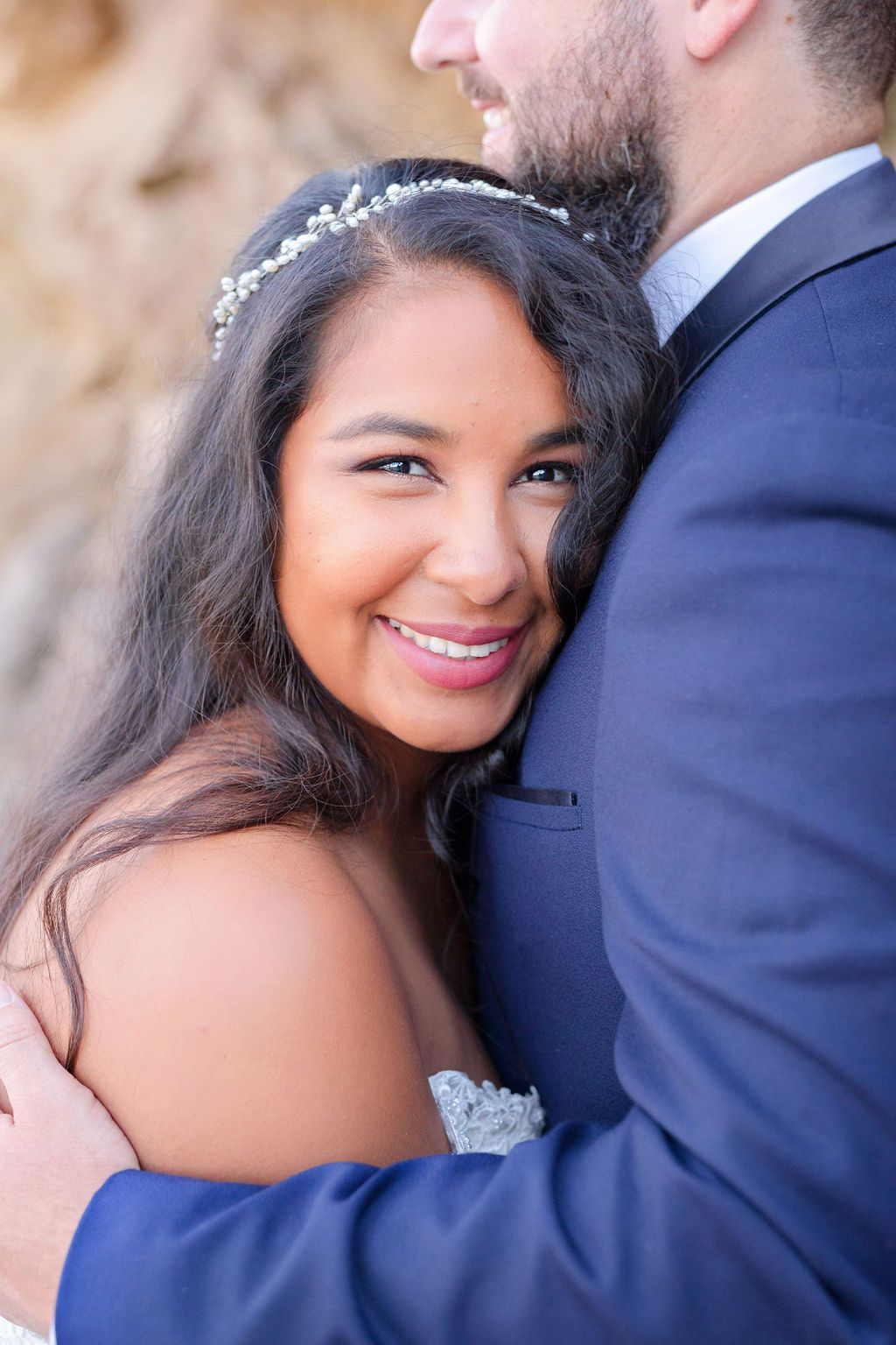 A close-up wedding portrait showing tender embrace against a blurred natural background.