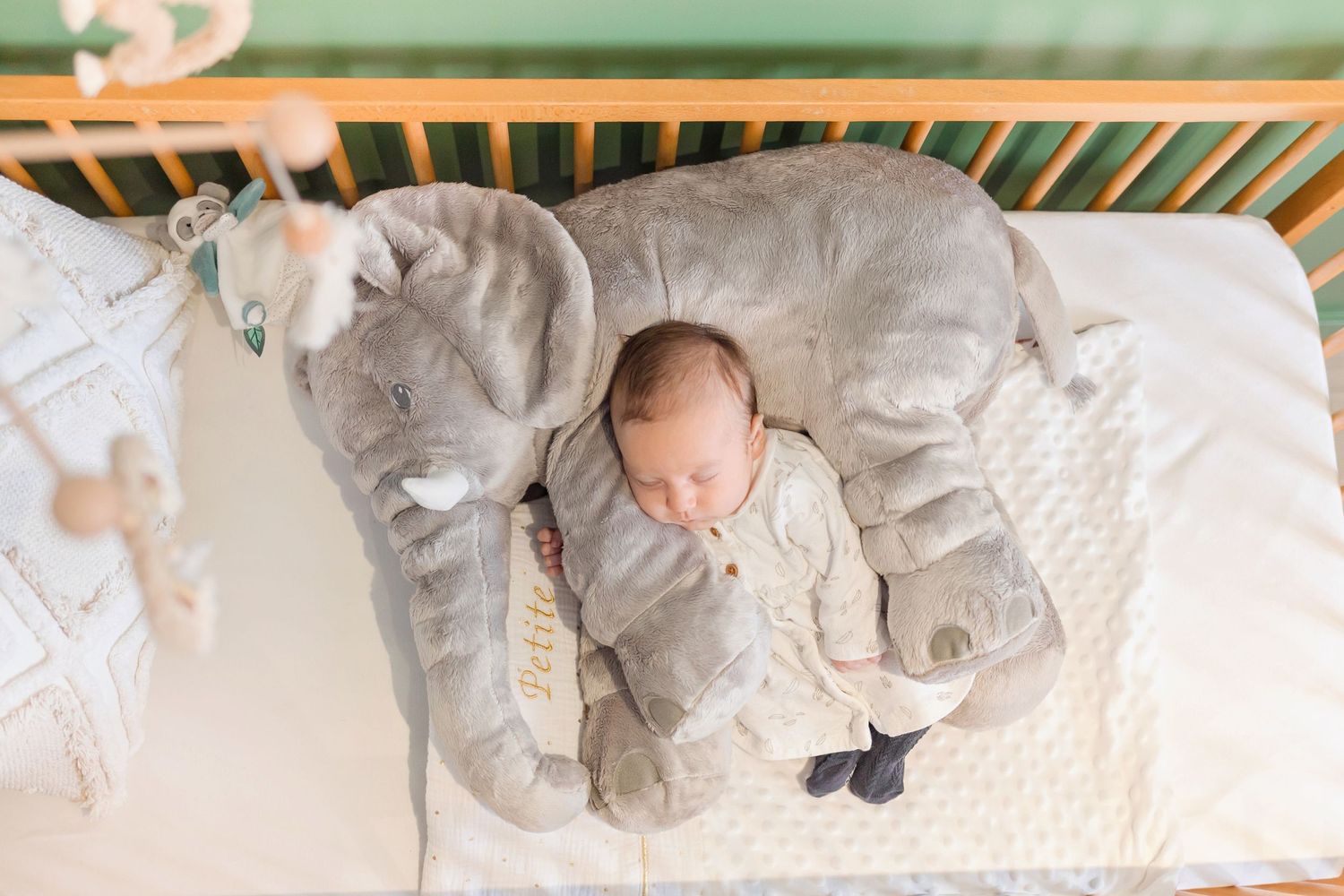 Infant sleeping peacefully between two plush elephant pillows in wooden crib.