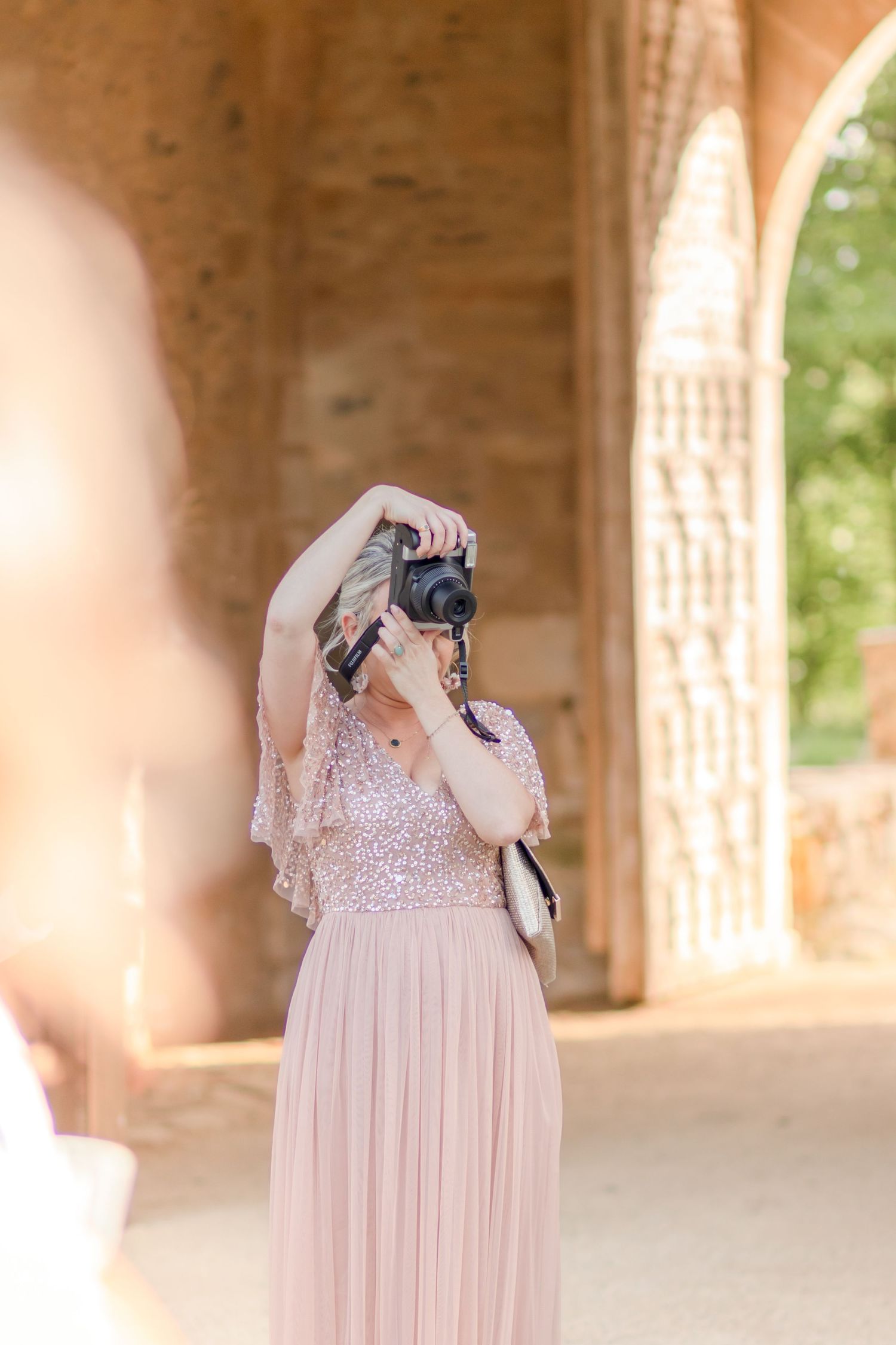 Person wearing a blush pink gown with delicate lace details in an outdoor setting.