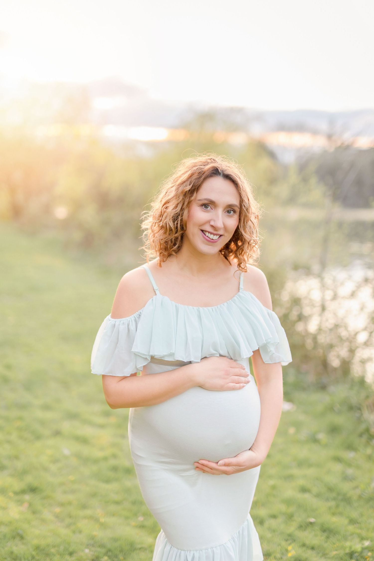 Glowing sunset maternity portrait with a light blue ruffle dress in a grassy field.