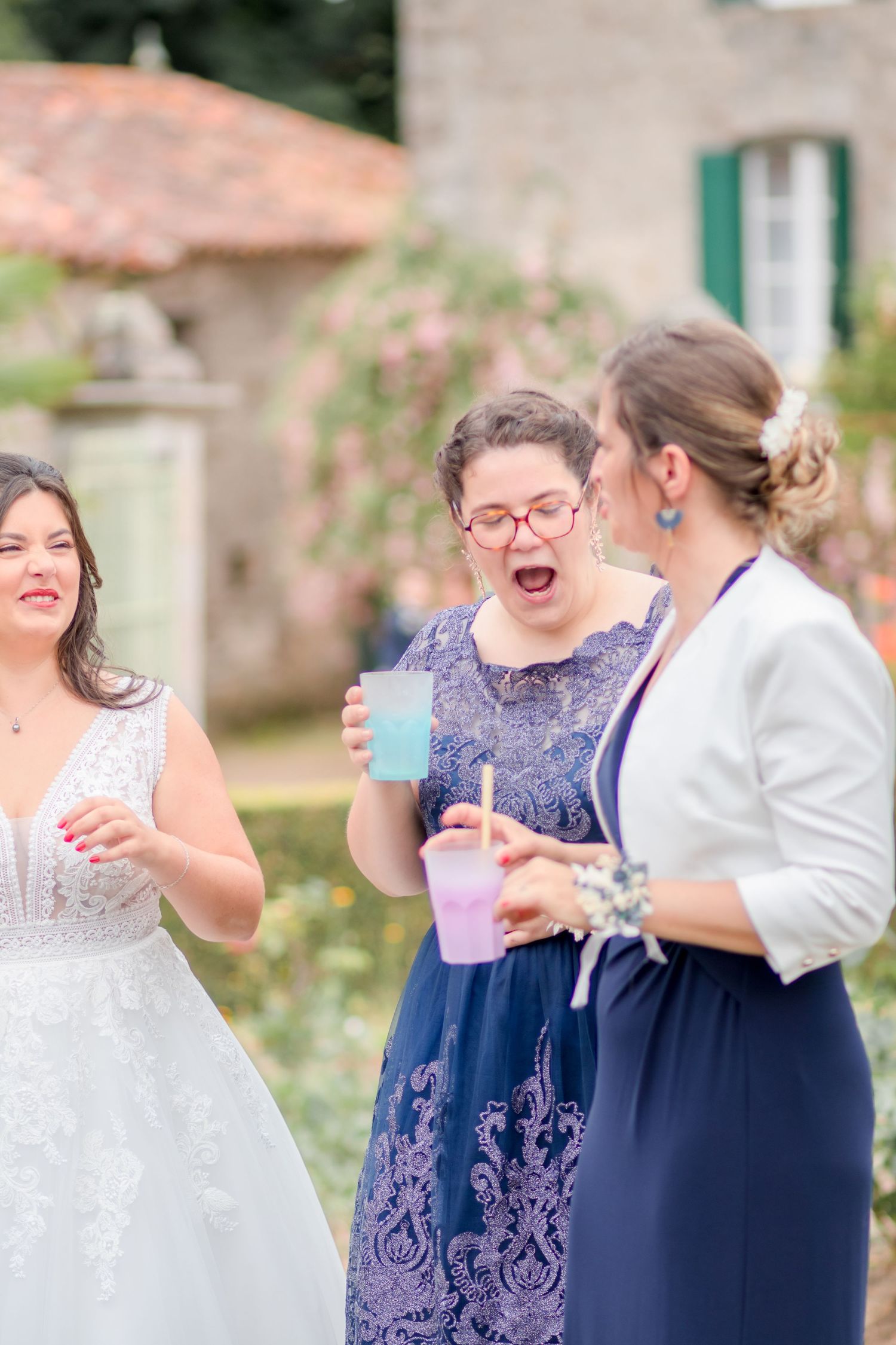 Joyful wedding party members sharing drinks and laughter in a garden setting.