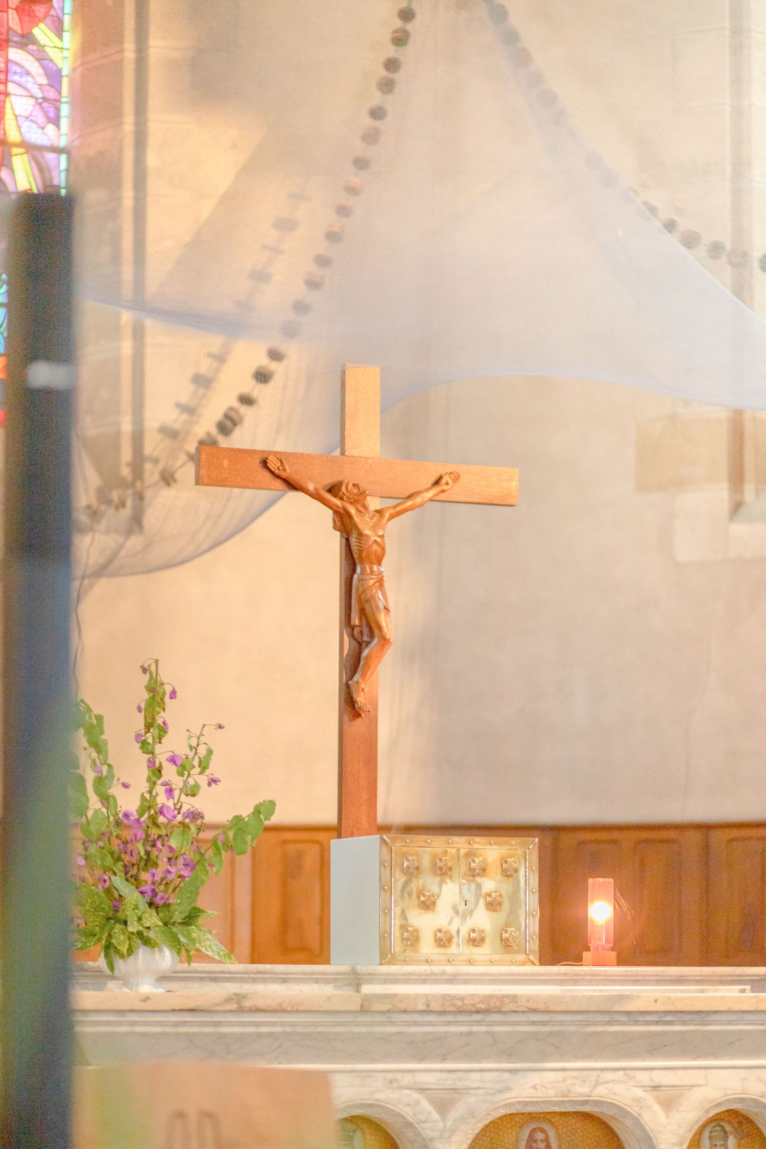 Church altar with wooden crucifix and floral arrangements in soft natural light.