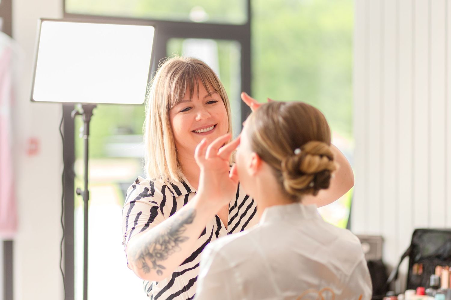 Makeup artist in zebra print dress applies cosmetics in bright studio setting.