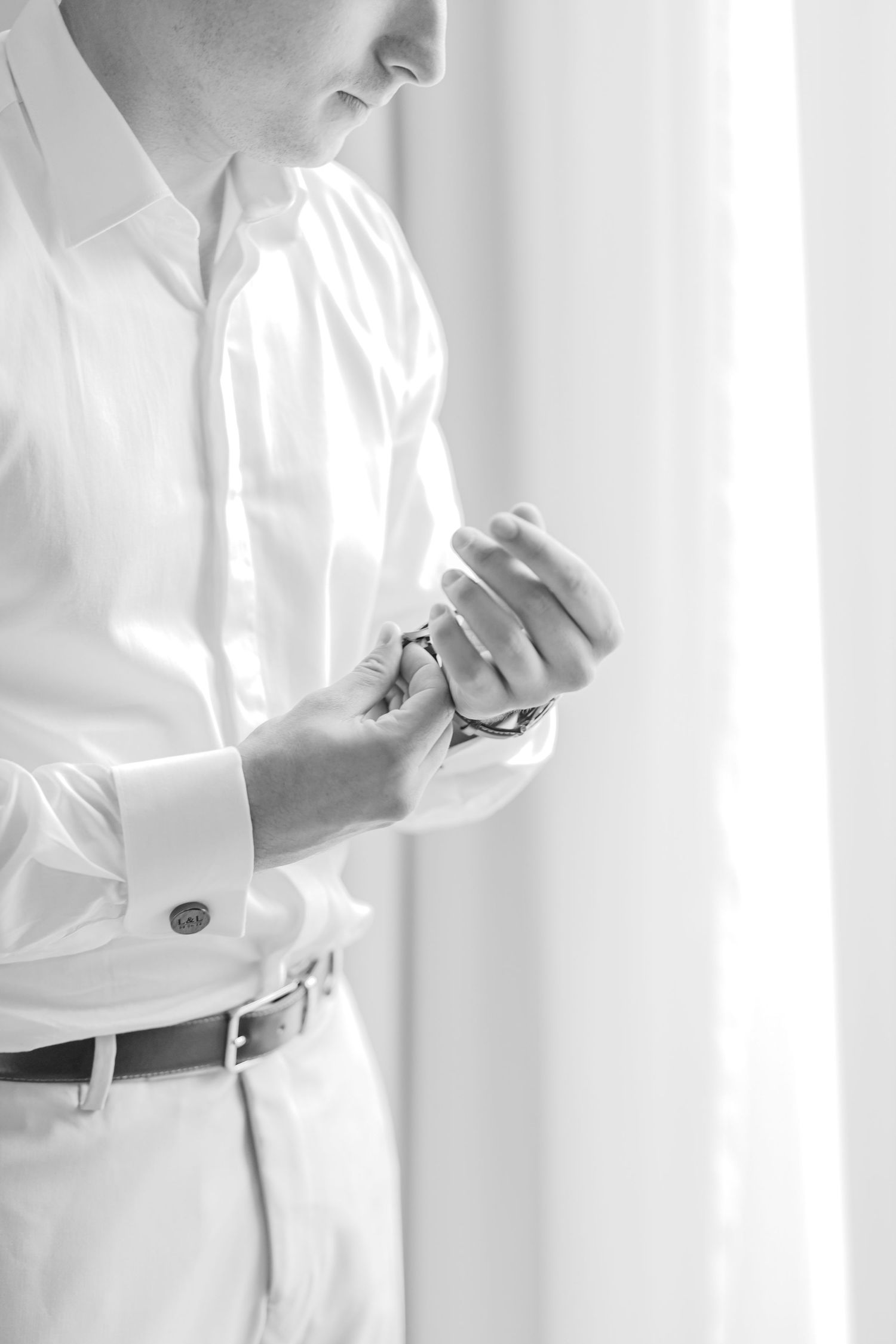 Close-up of formal white attire being adjusted against a bright window.