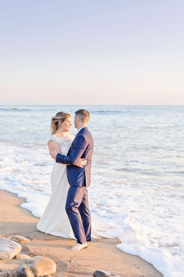 Newlyweds embracing by ocean waves during beach wedding photoshoot.