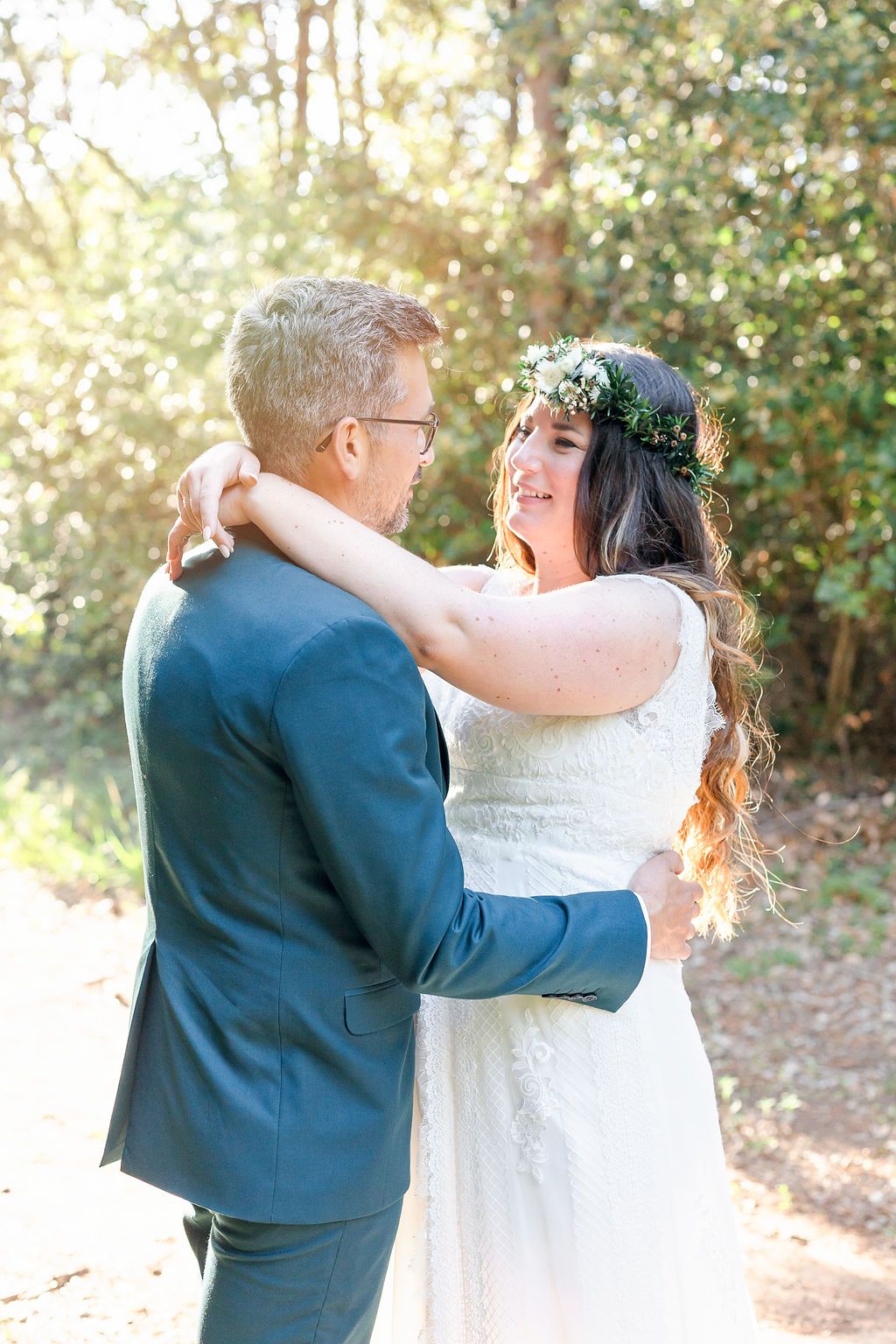 Wedding couple shares joyful embrace in dappled sunlight beneath forest canopy.