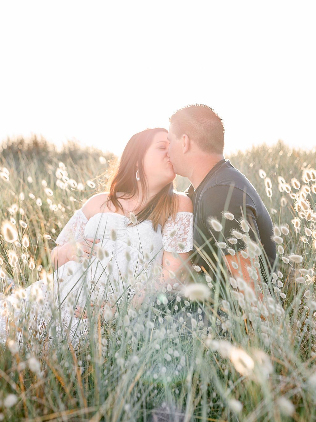 A couple shares a tender moment among tall grass and white wildflowers.