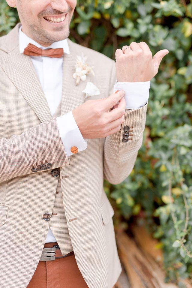 Elegant beige suit jacket with wooden bow tie and boutonniere detail.