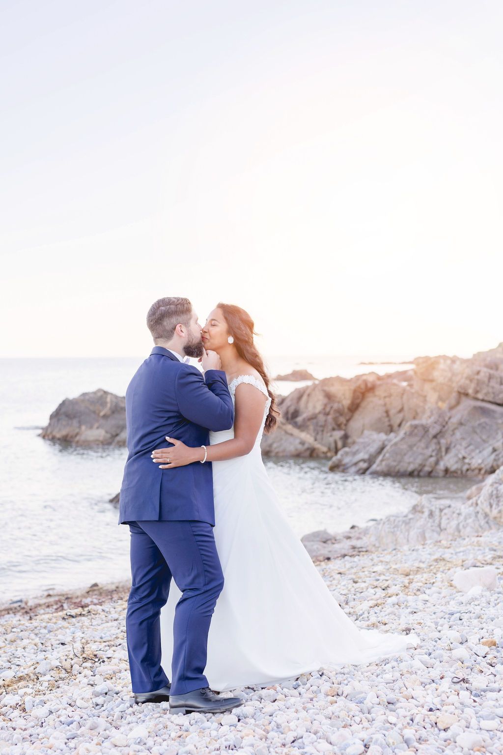 Newlyweds share an intimate moment on a rocky beach during golden hour.