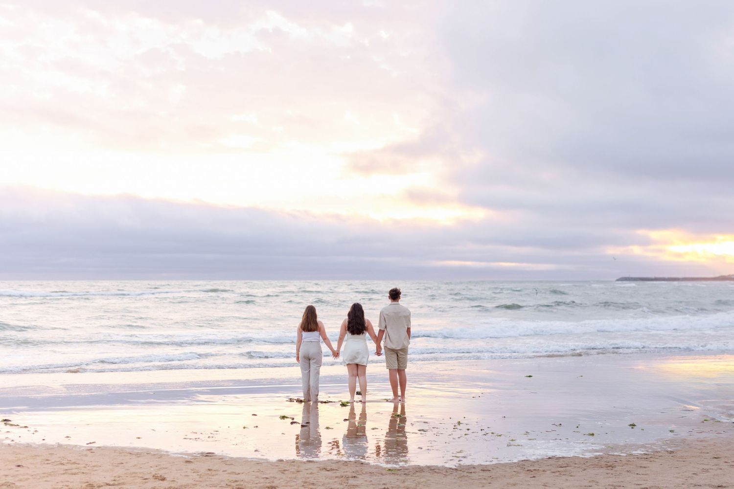 Three people standing at the ocean's edge during a beautiful sunset.