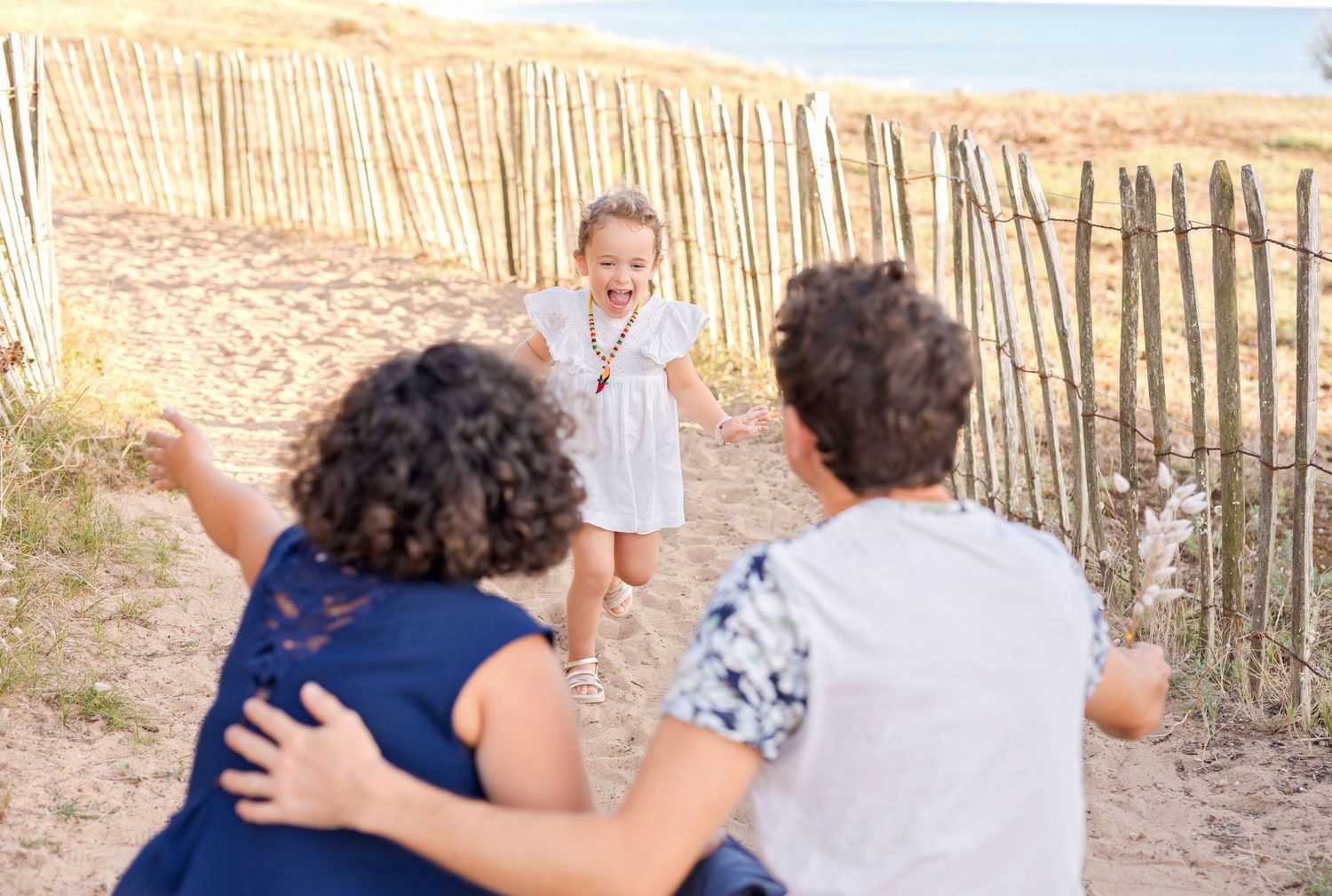 Running and playing together at a sandy beach with wooden fence in the background.