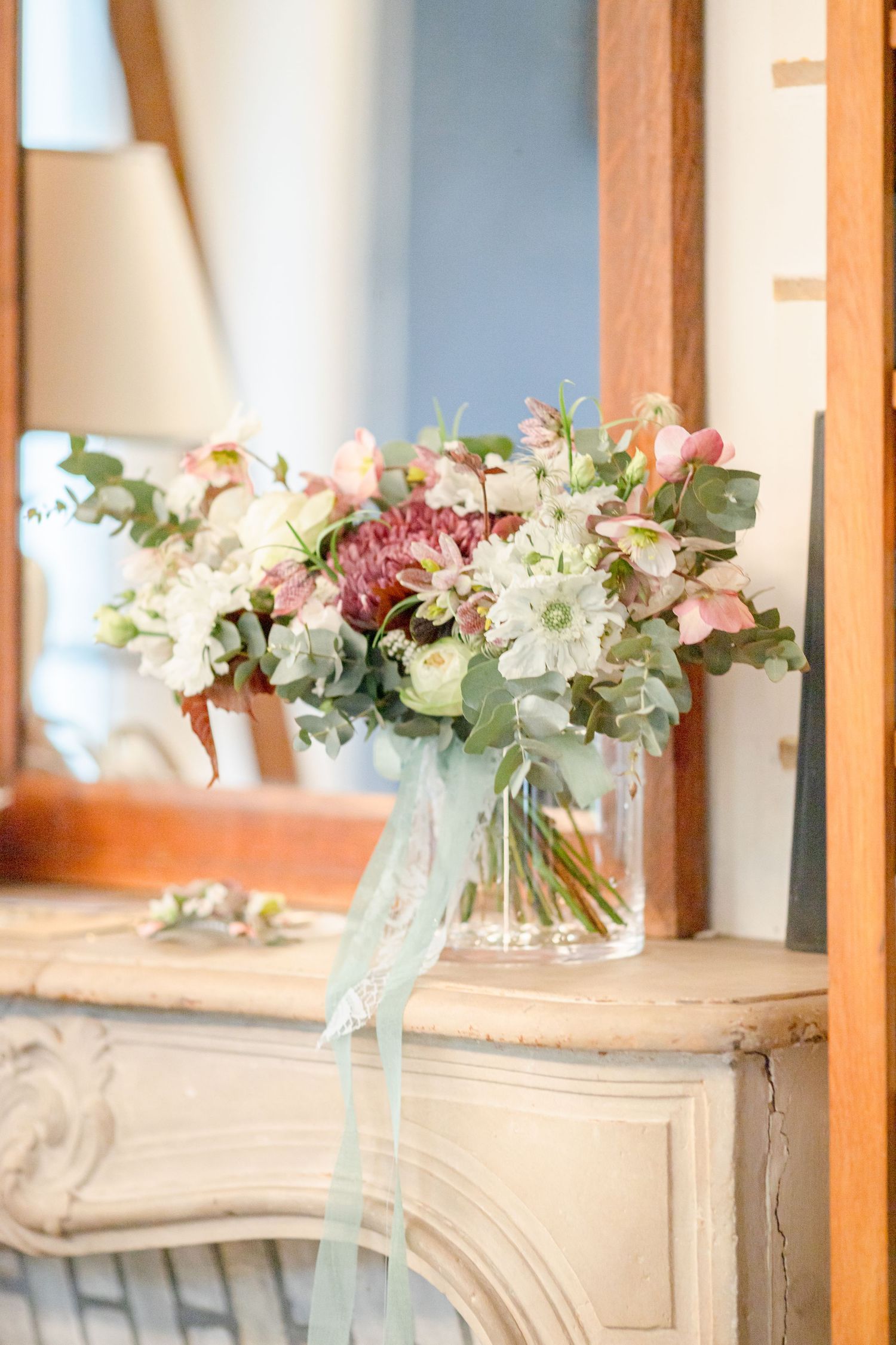 Romantic pastel flower arrangement with mint ribbon in glass vase on vintage cabinet.