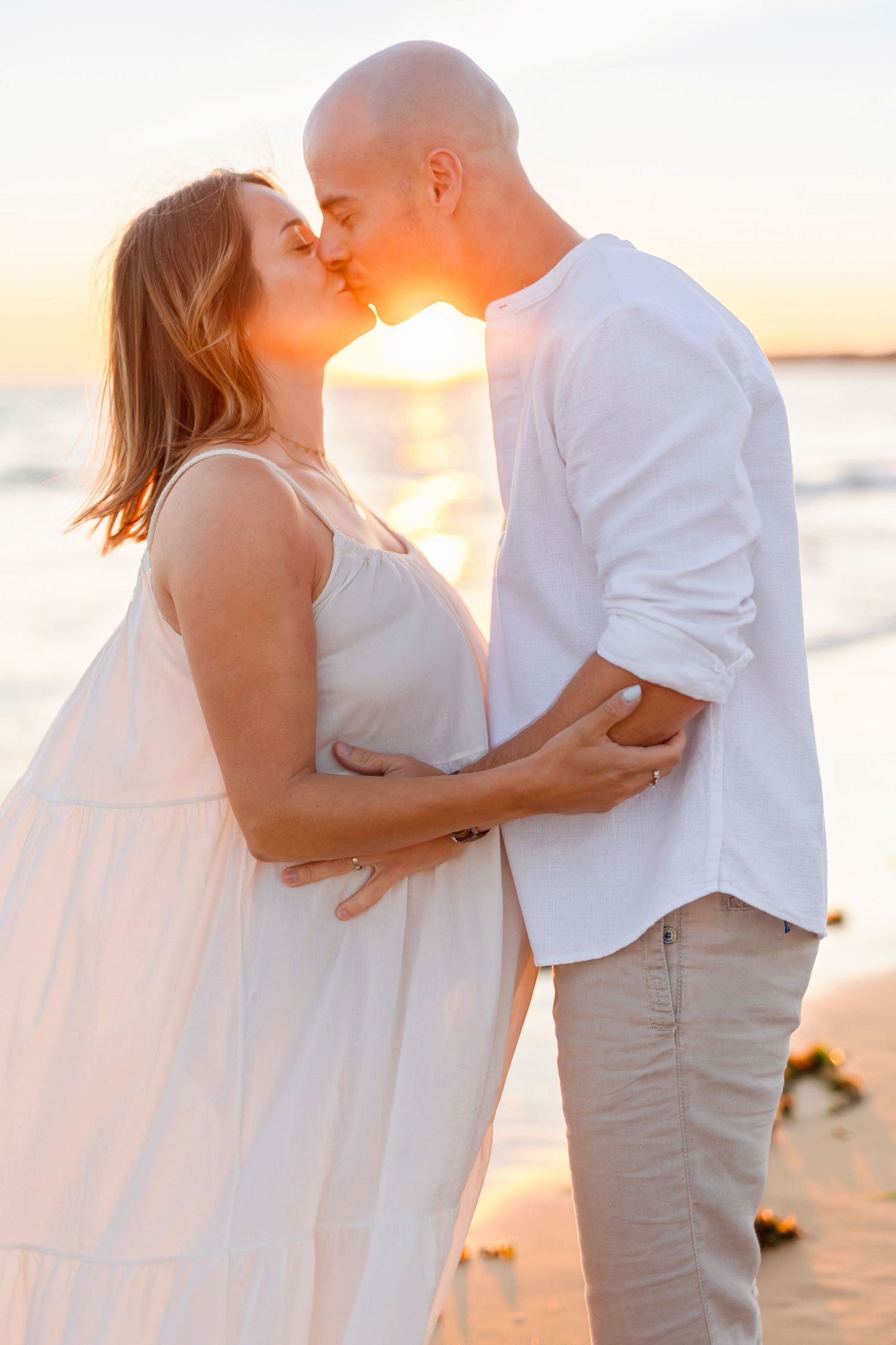 Romantic beach sunset portrait of couple in white and beige outfits.