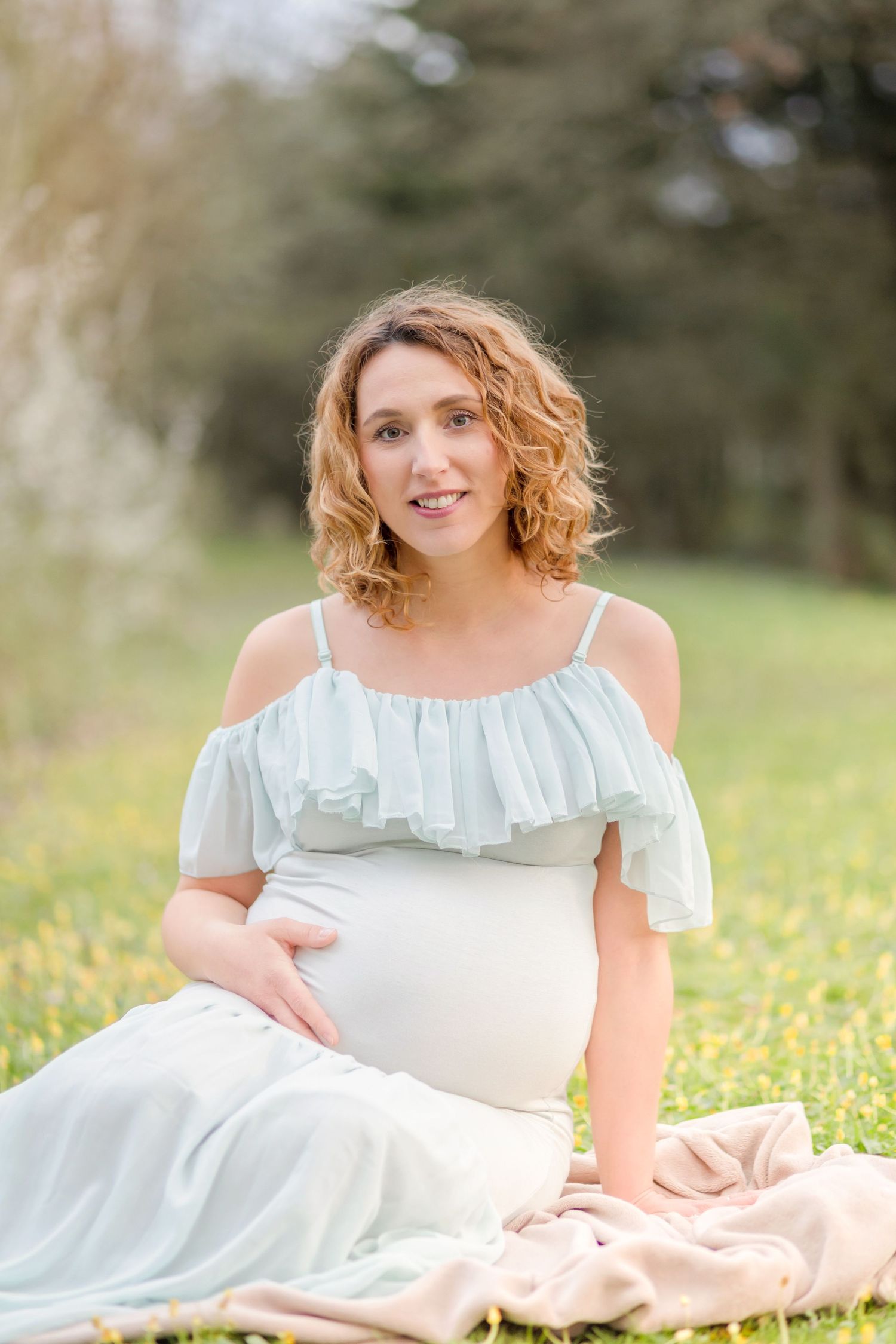Glowing maternity portrait in a pale blue ruffle dress amidst a spring meadow.