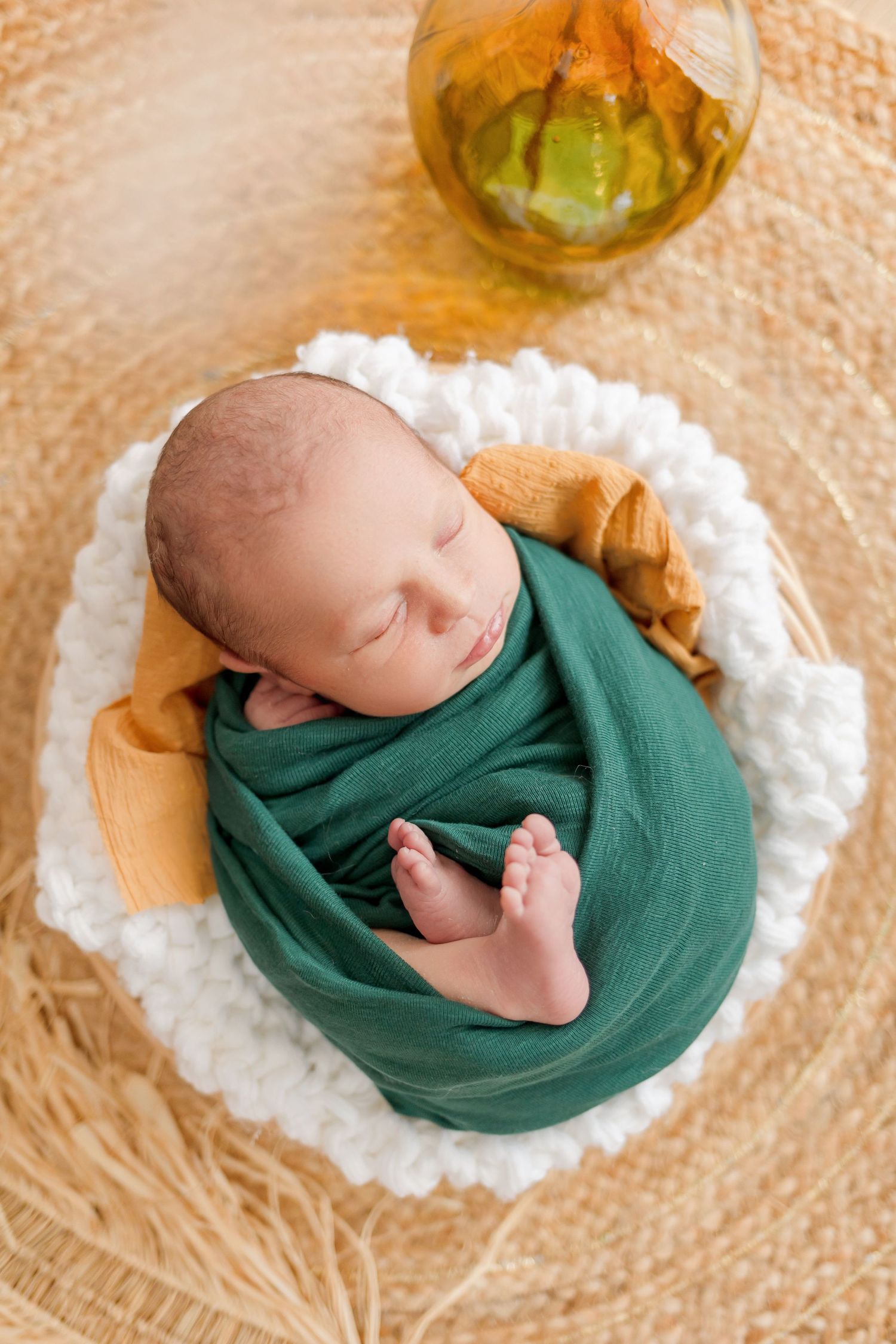 Sleeping newborn in green wrap lying in circular nest with decorative gold glass accent.