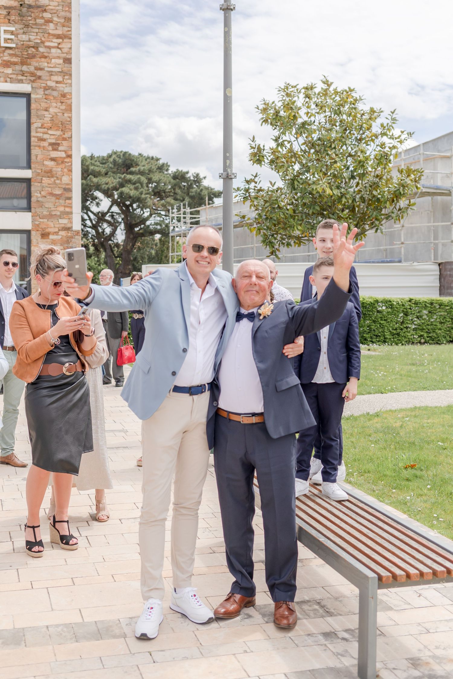 Wedding guests gather outdoors near brick columns posing for candid photos.