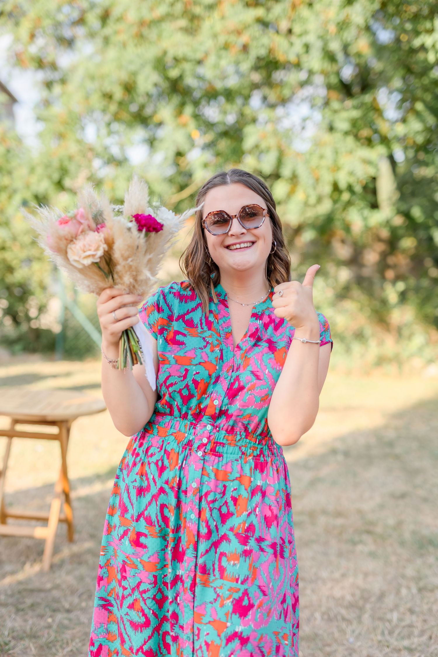 Guest in floral dress enjoys refreshments at sunny outdoor wedding reception.