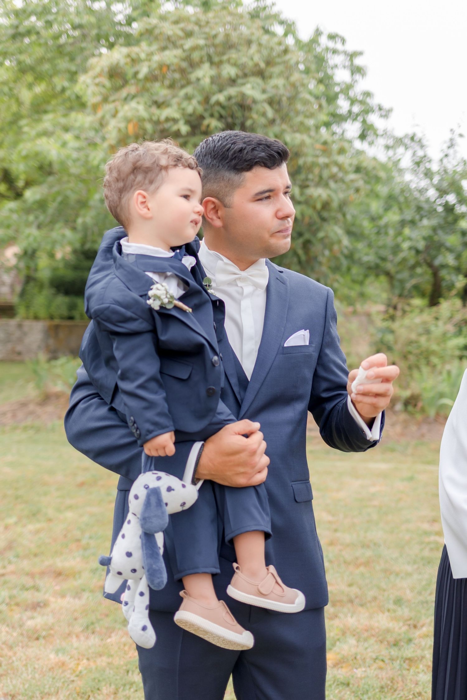 Young boys in navy suits standing together at an outdoor event.
