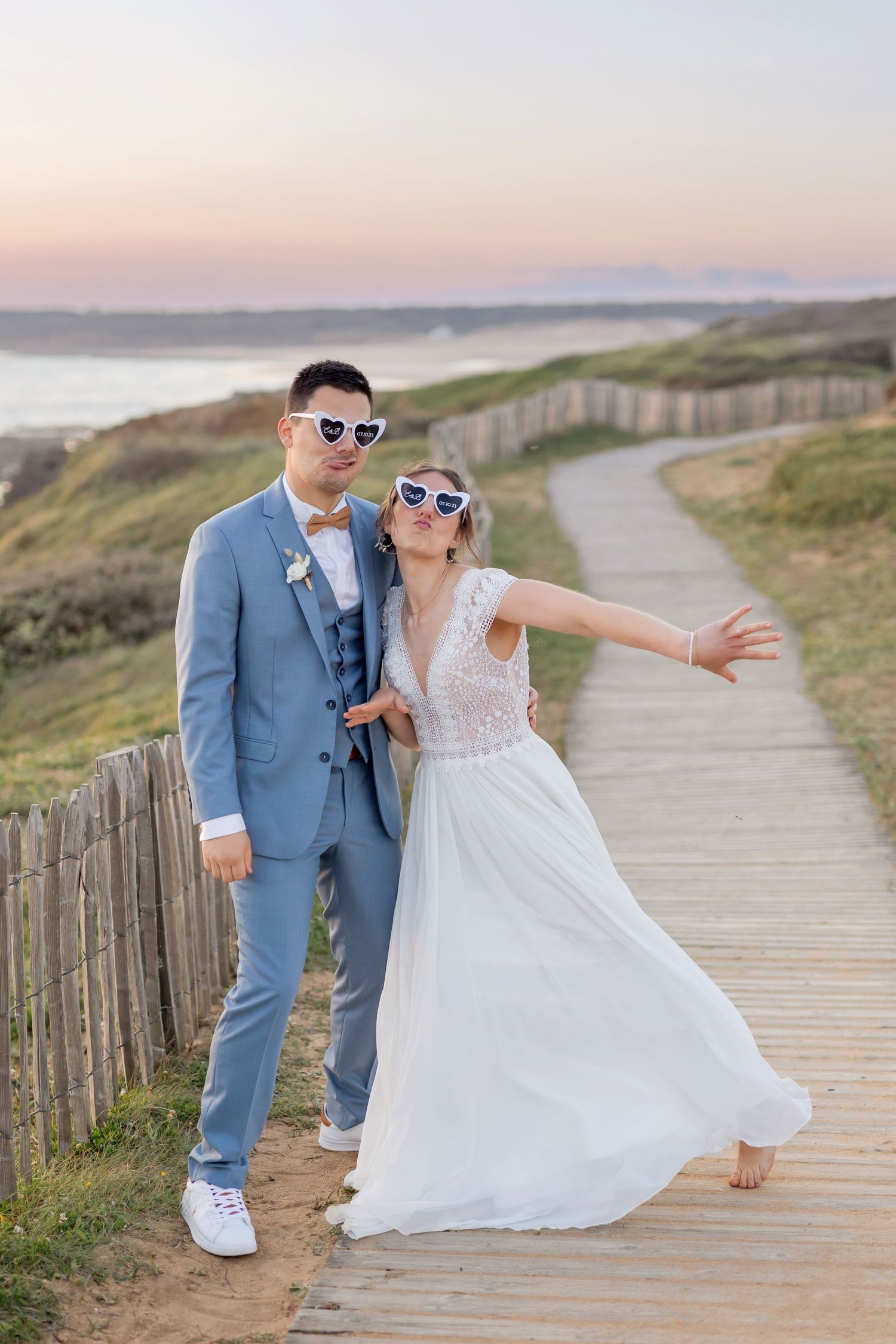 Fun wedding photo with couple wearing sunglasses on coastal boardwalk.