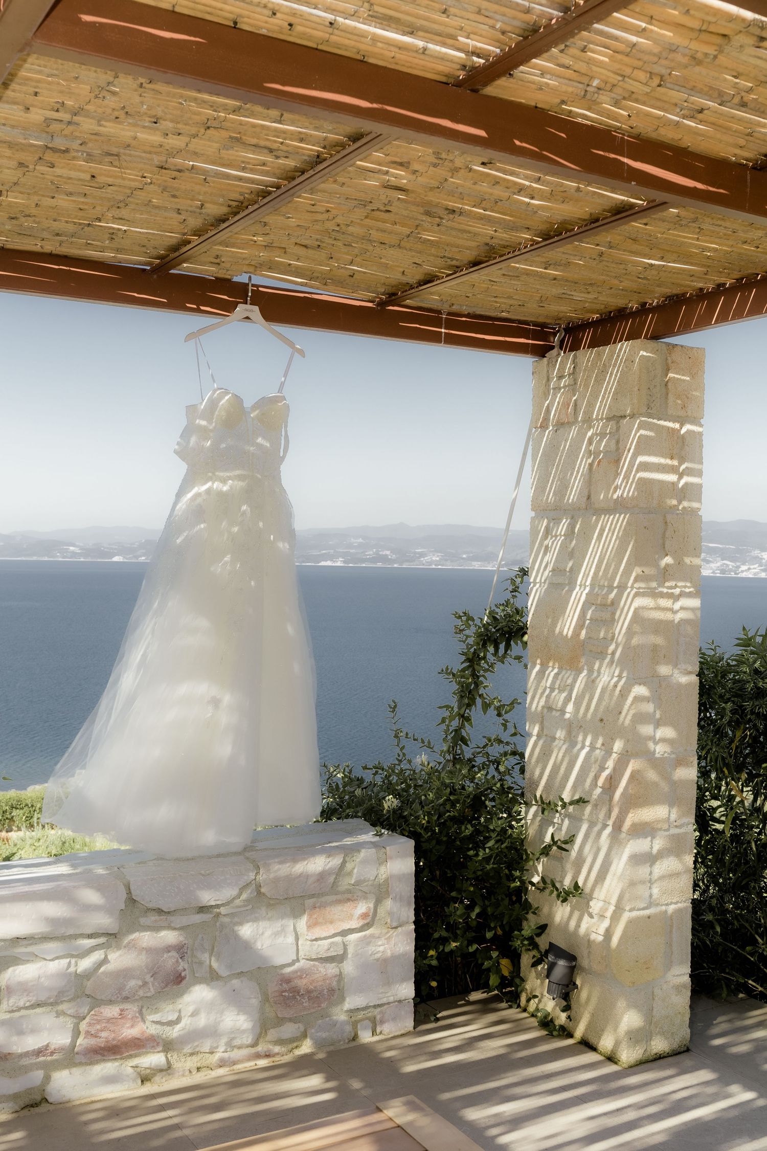 White wedding dress hanging under wooden pergola with ocean view.