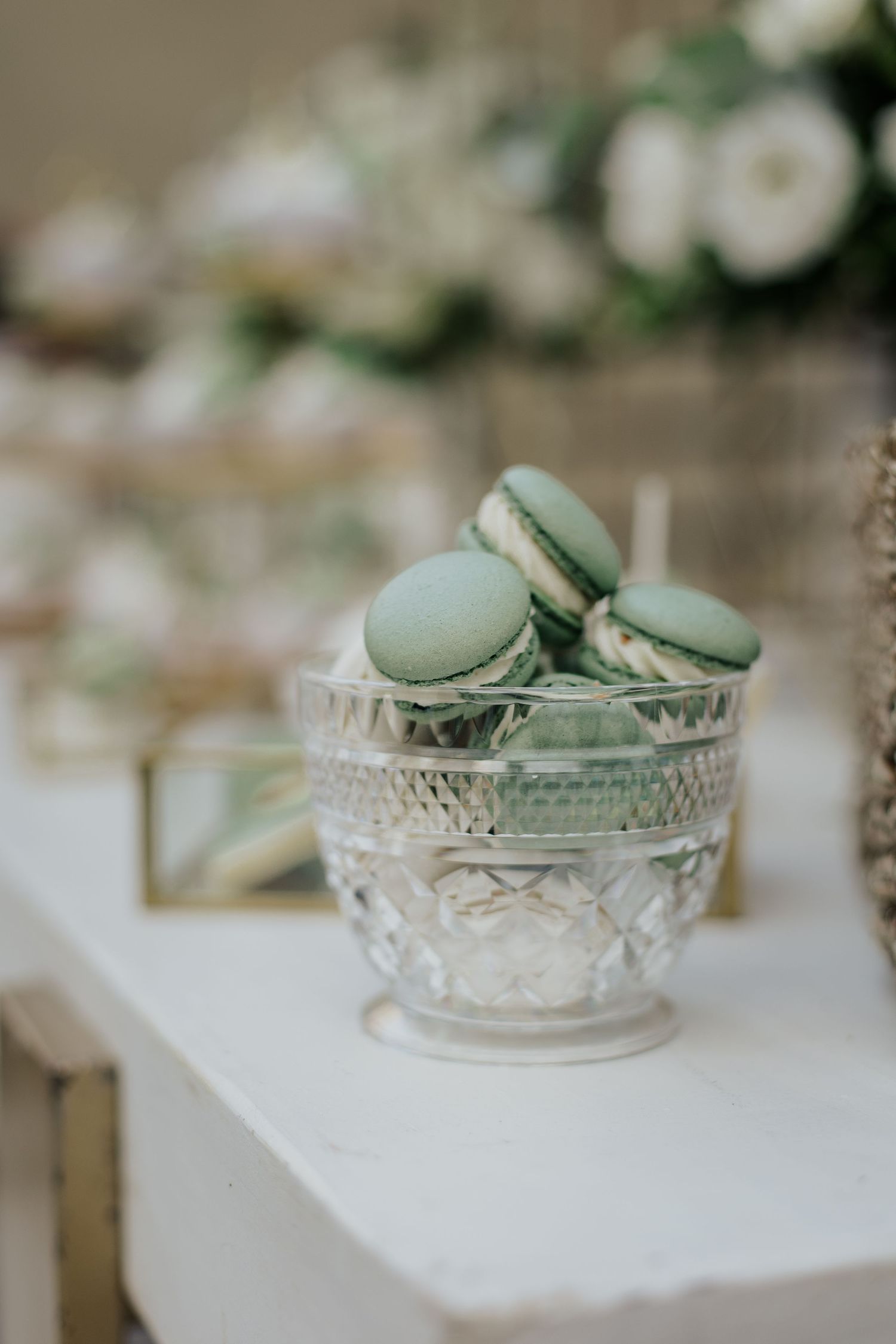 Mint green macarons displayed in an elegant crystal glass bowl on a white surface.