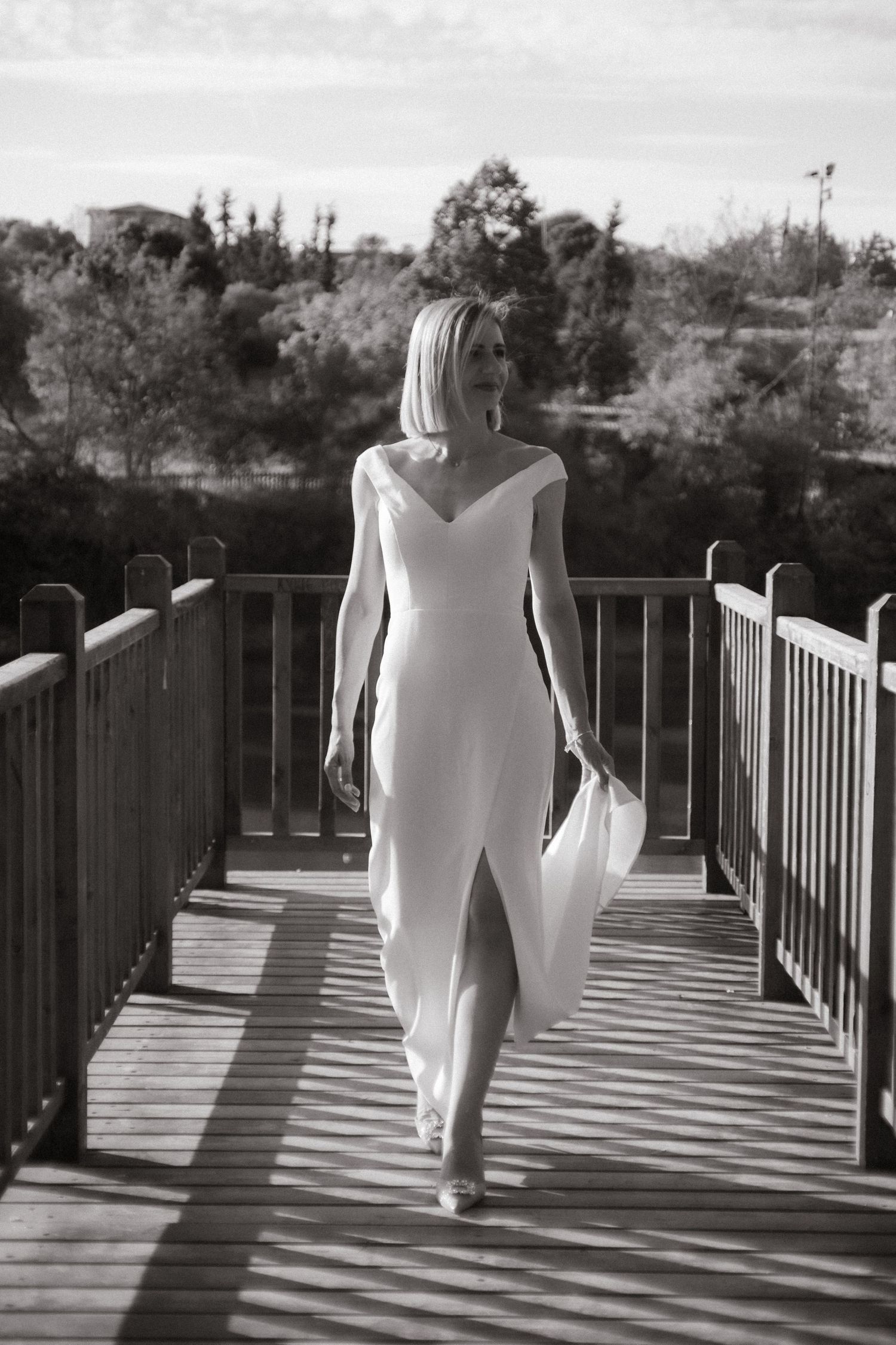 Black and white photo of someone walking on a wooden bridge in white attire.