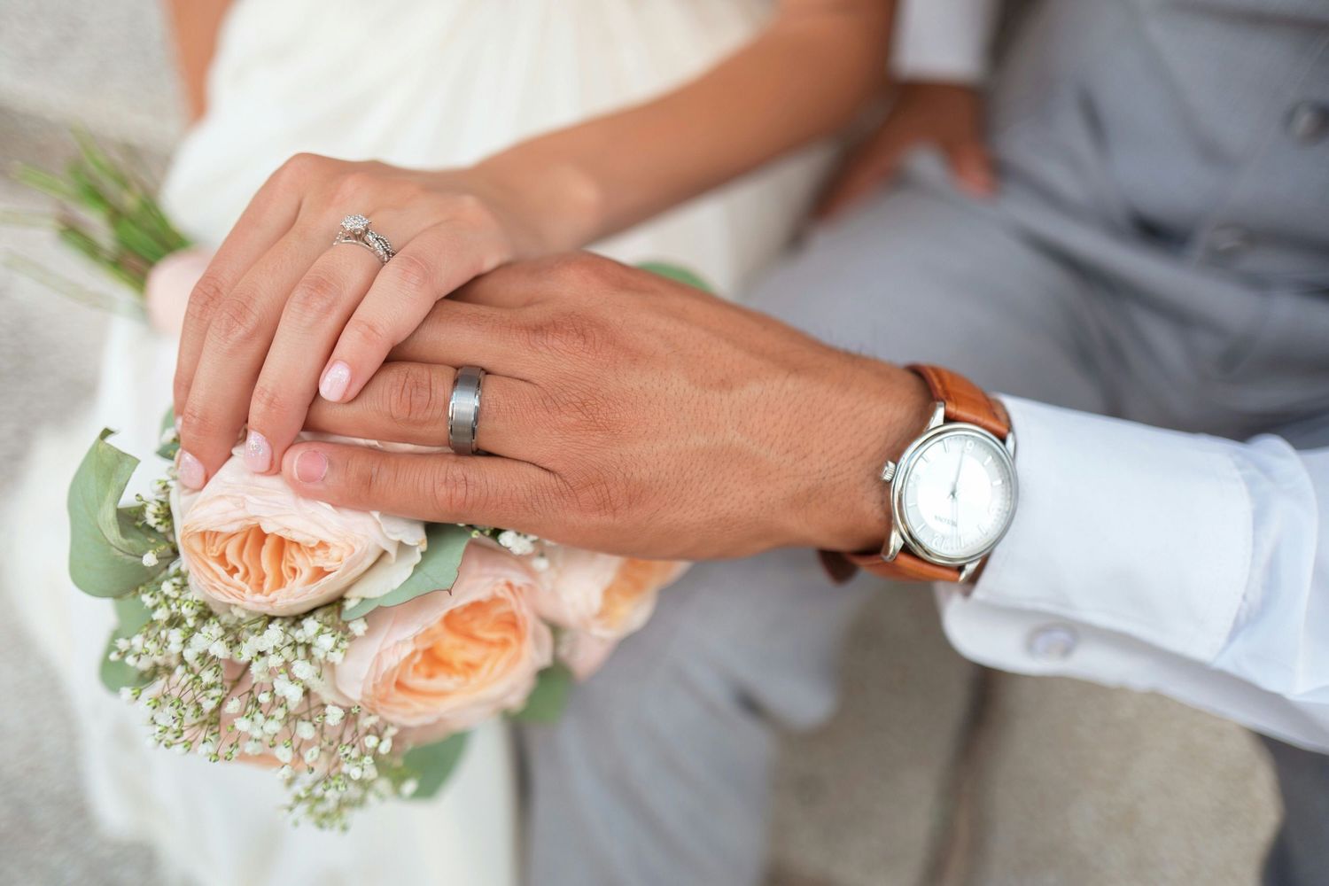 Close-up of wedding rings and delicate floral details with hands in frame.