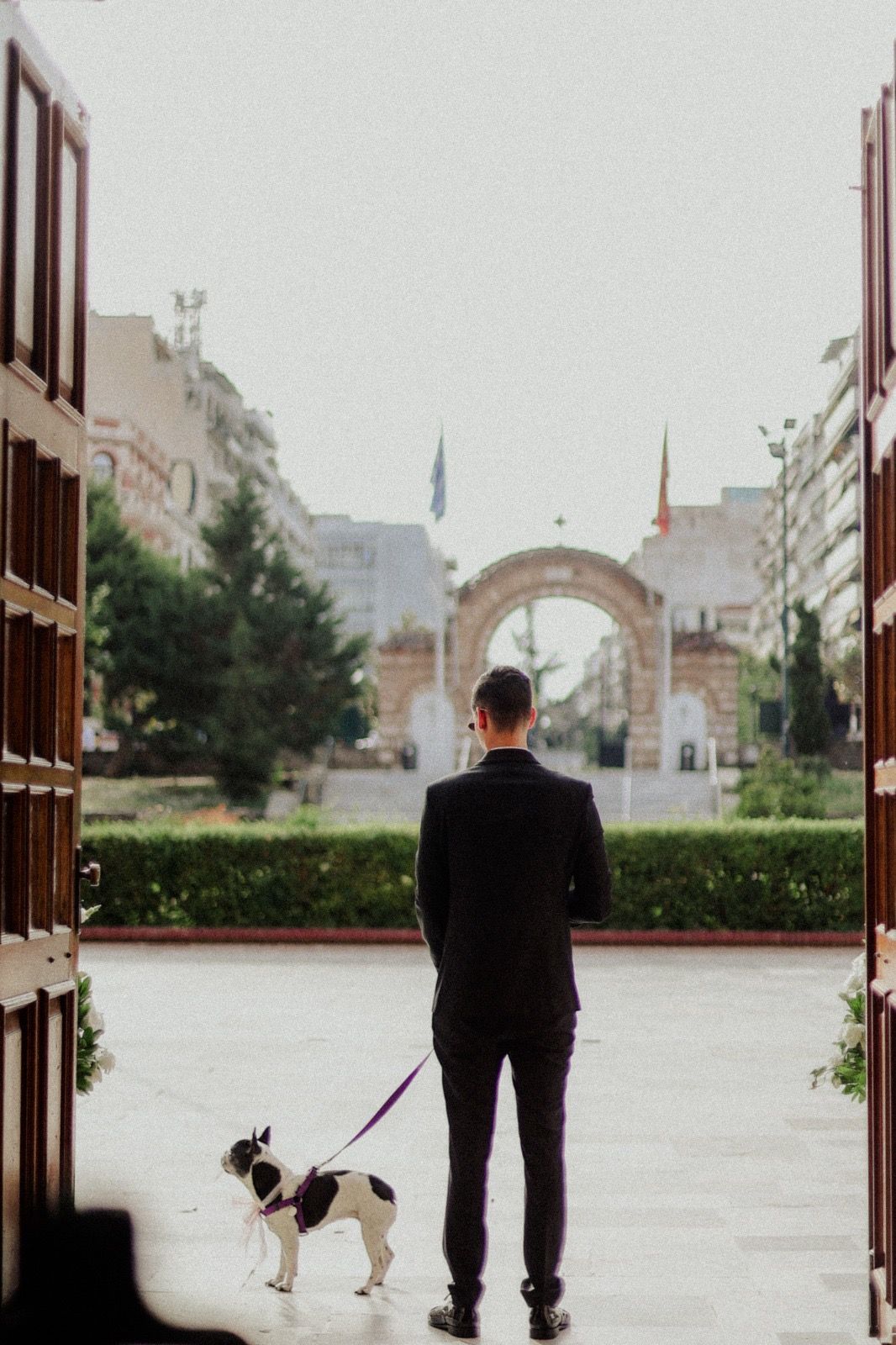 Person in dark suit walking dog on leash near brick building.