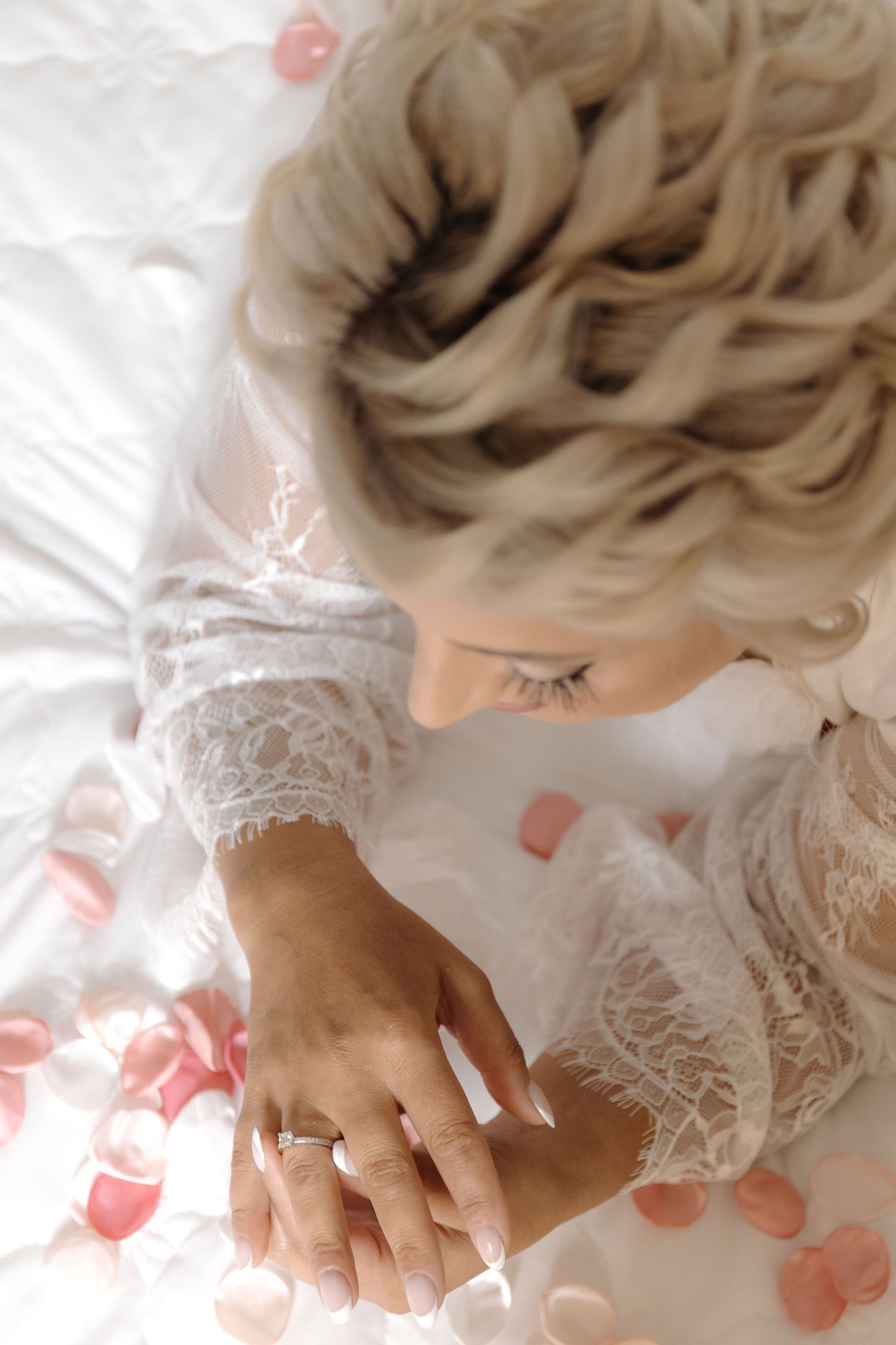 Delicate bridal detail shot showing lace sleeves and wedding ring among rose petals.