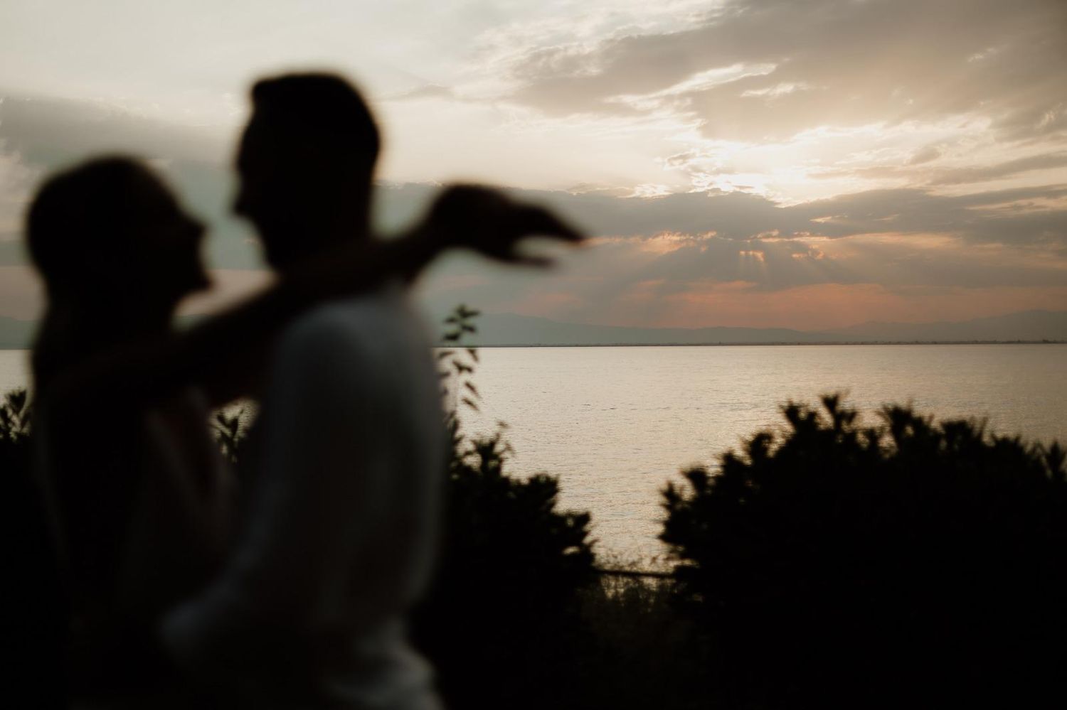 Silhouette of couple against sunset over water with dramatic sky.