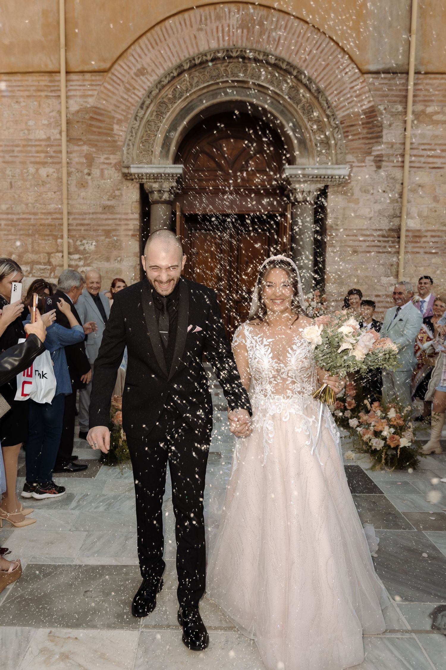 Joyful wedding celebration with confetti outside a historic brick church entrance.