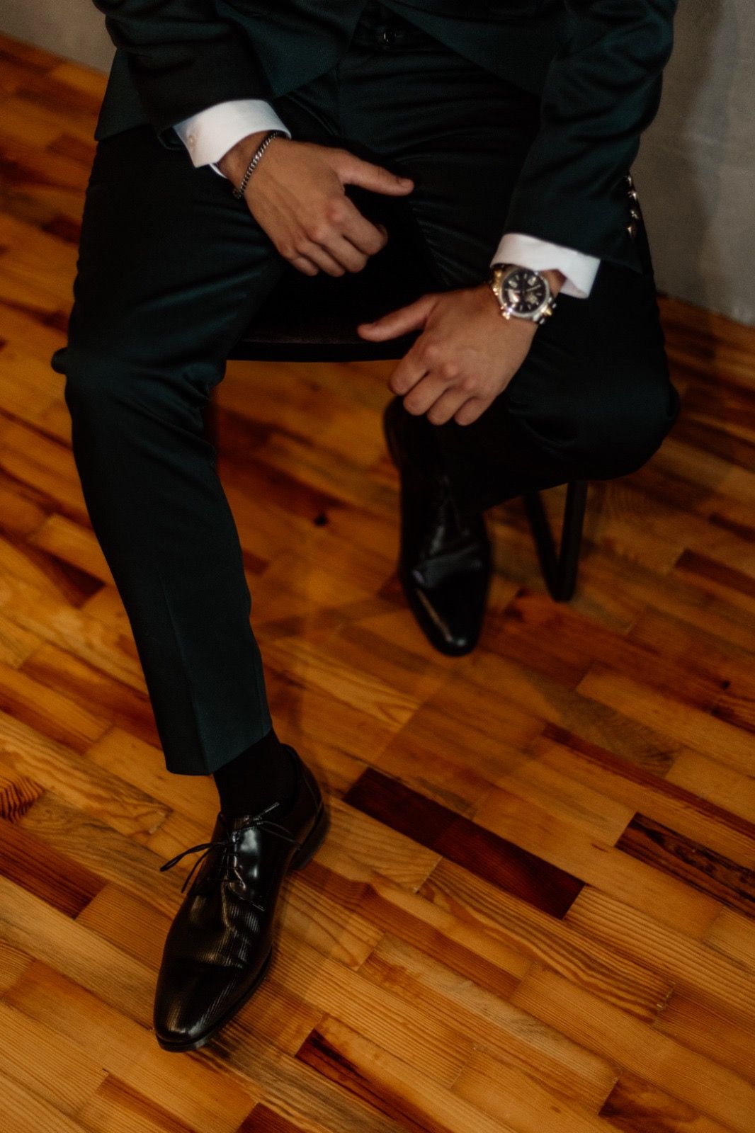 Close-up of formal black suit pants and polished dress shoes on hardwood flooring.