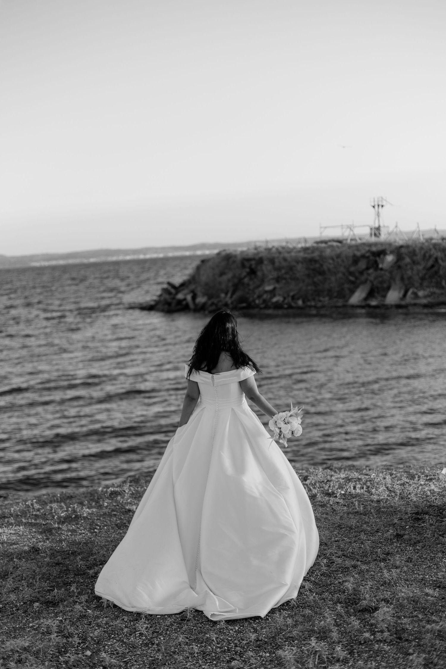 Wedding dress silhouette against coastal cliff landscape in black and white.