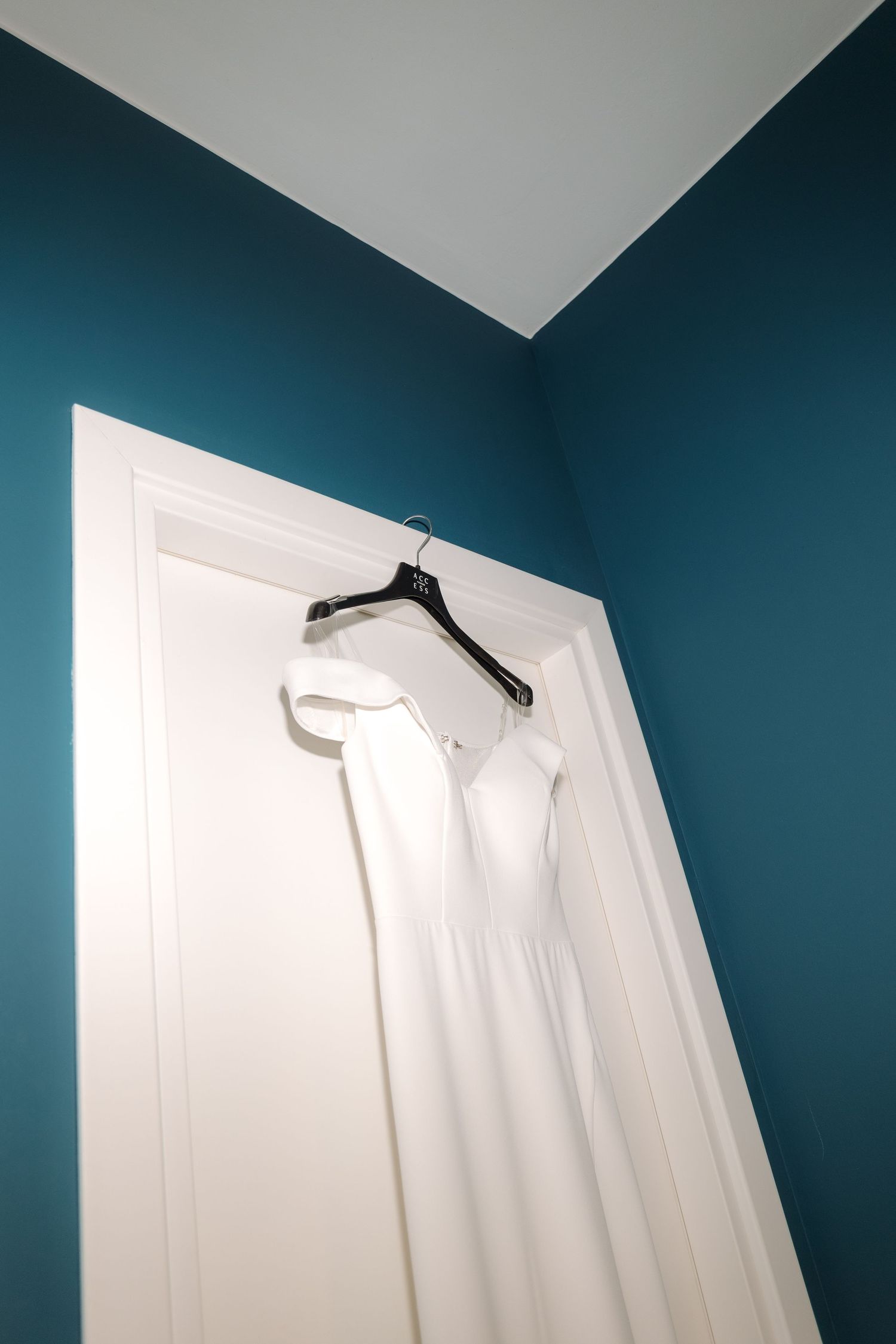 White dress shirt hanging on hanger against teal blue wall.