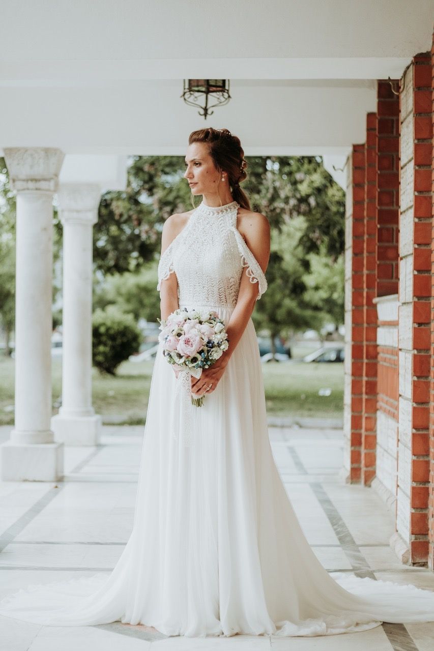 Bride in halter neck lace gown holding pink bouquet on columned porch.