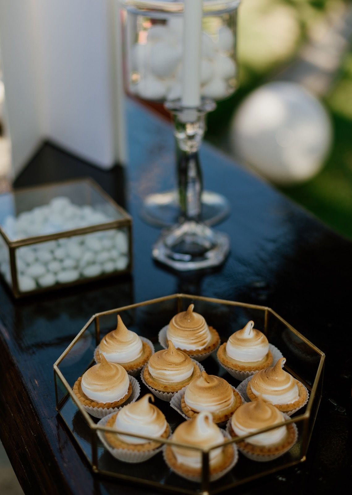 Elegant dessert display featuring mini cupcakes with golden meringue tops on dark surface.
